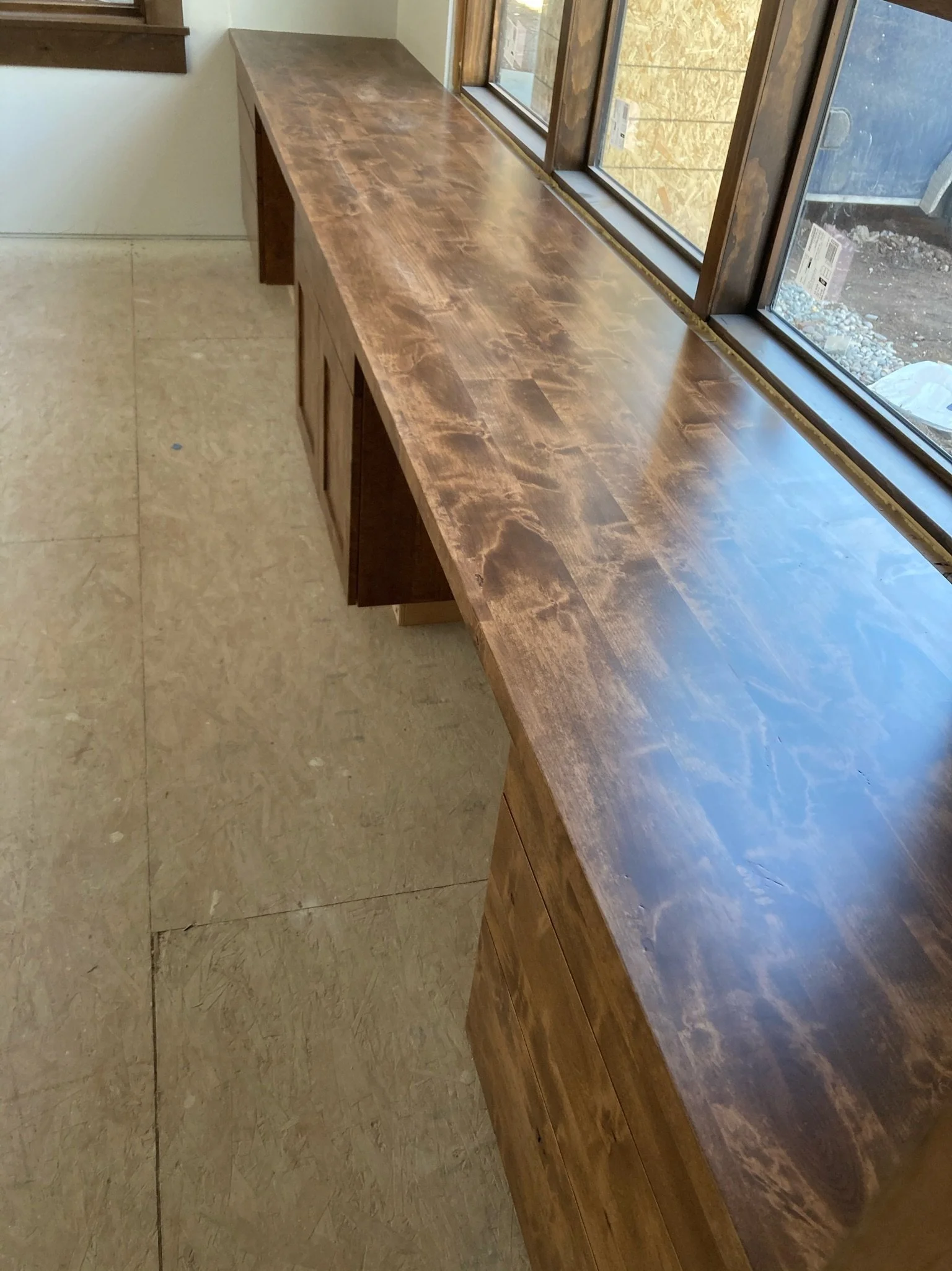 A long wooden countertop near a large window, with a view of a parking lot outside.