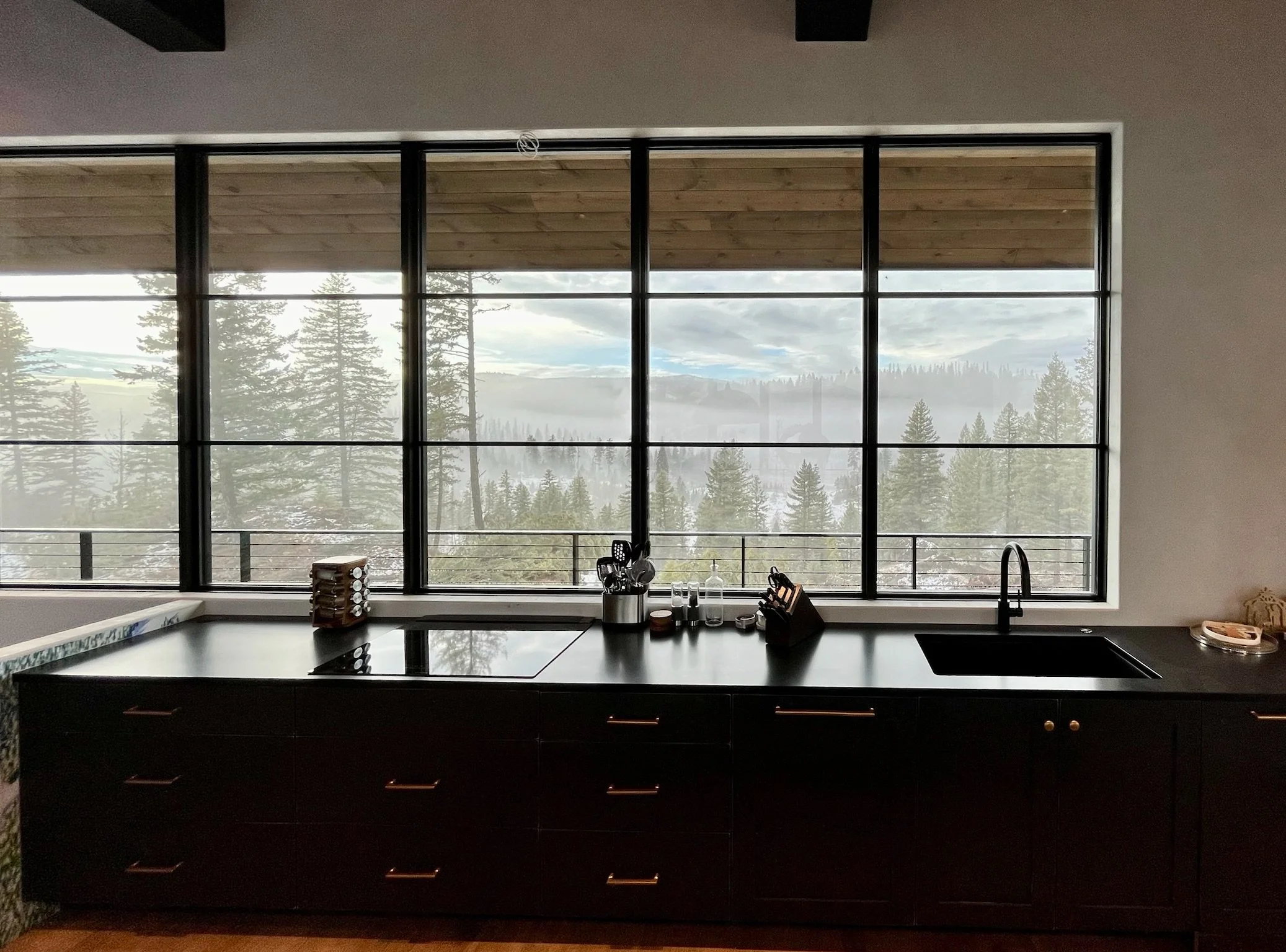 Kitchen with large window showing a view of trees and mountains, dark cabinetry, and a black countertop with kitchen utensils and soap dispenser.