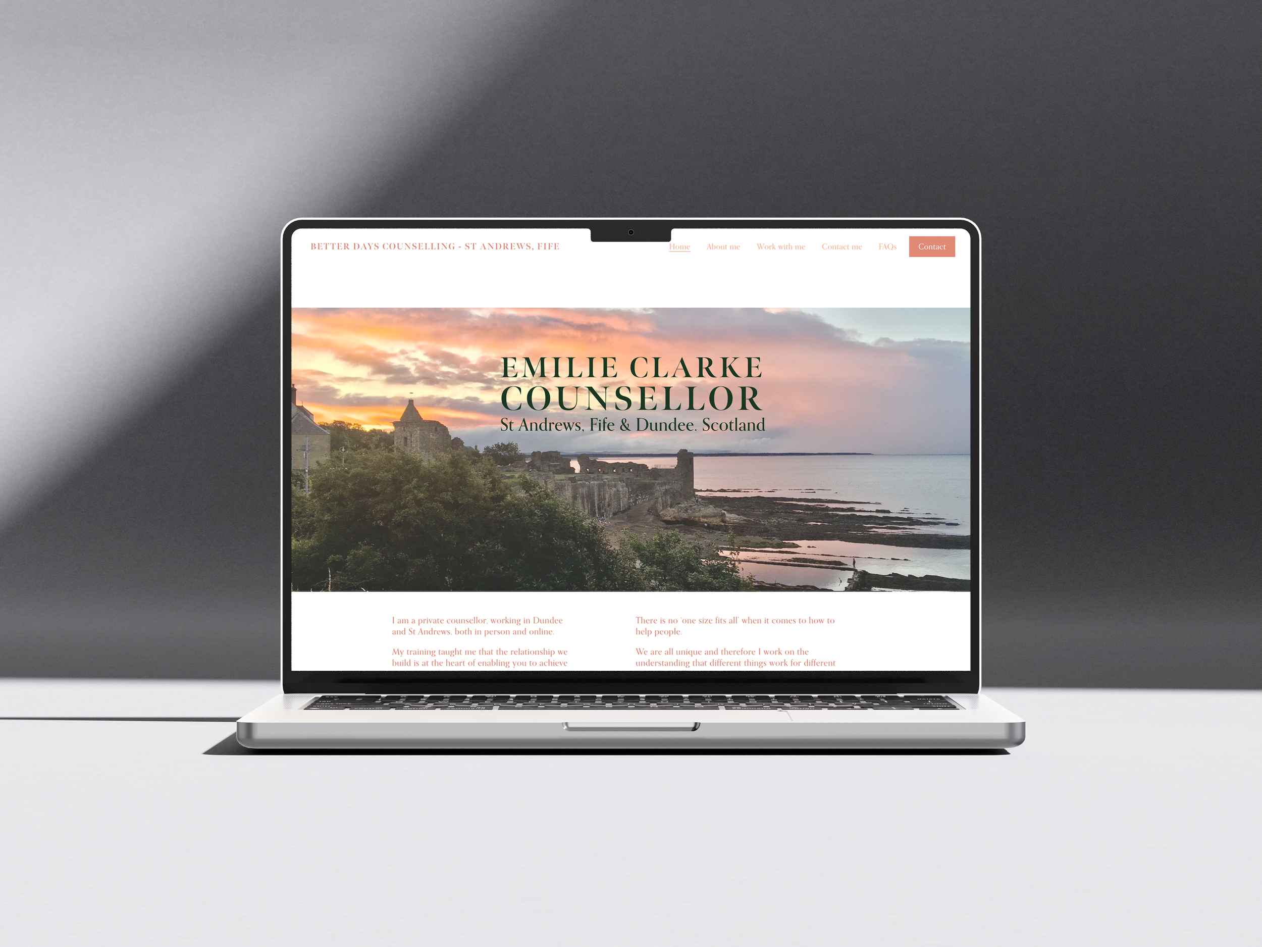 Laptop displaying a website for Emile Clarke, a counselor in St Andrews, Fife, Scotland. The website features a scenic sunset view of a coastline with historic buildings, a menu with options like Home, About me, Work with me, Contact me, FAQs, and a 