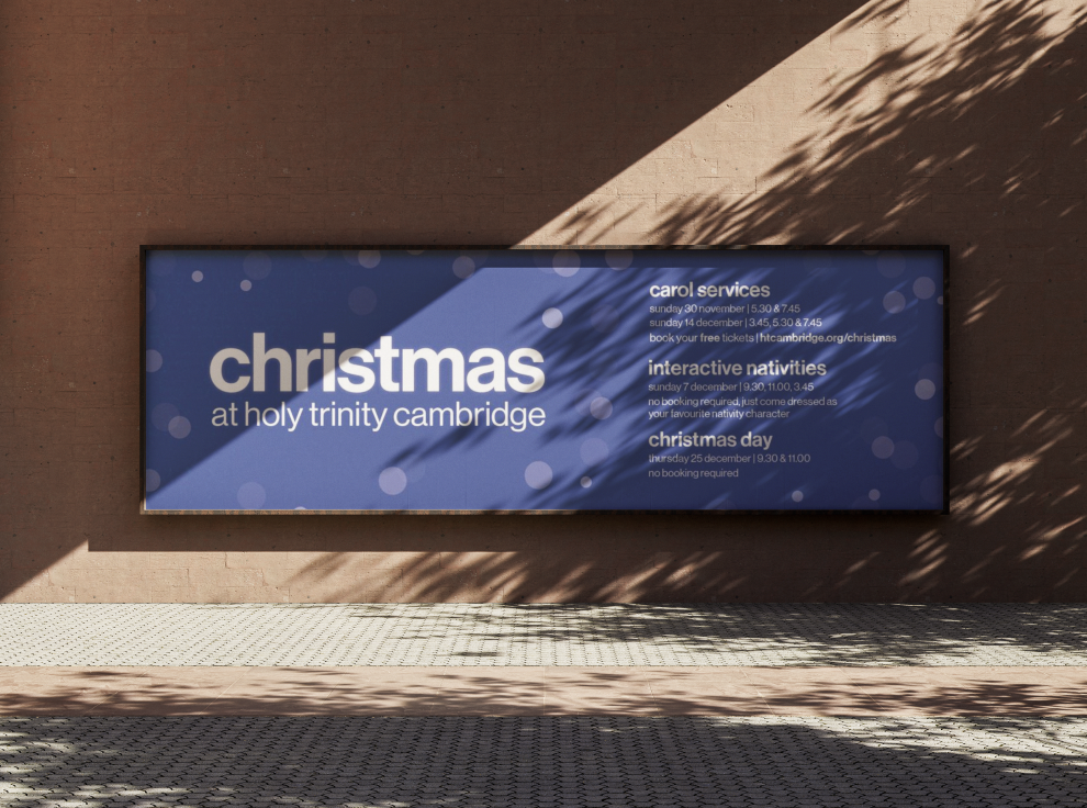 Blue banner on a brick wall advertising Christmas events at Holy Trinity Cambridge, including church services, interactive activities, and Christmas Day service, with details about dates, times, and booking information.