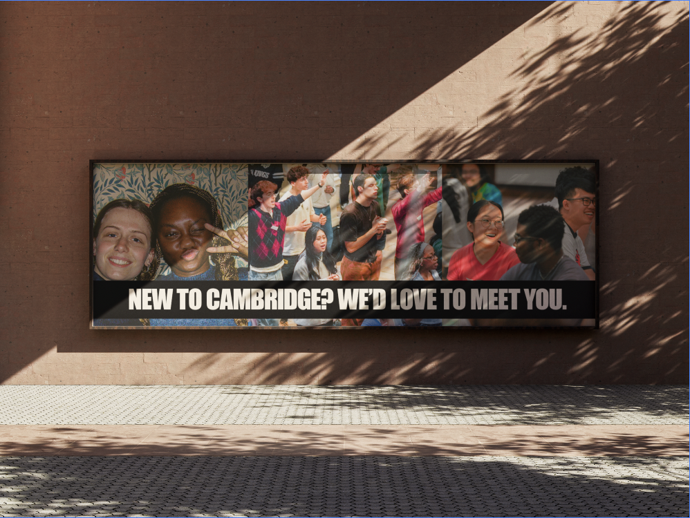 A billboard on a brick wall displaying photos of diverse groups of new students and a message that reads, 'New to Cambridge? We'd love to meet you.'