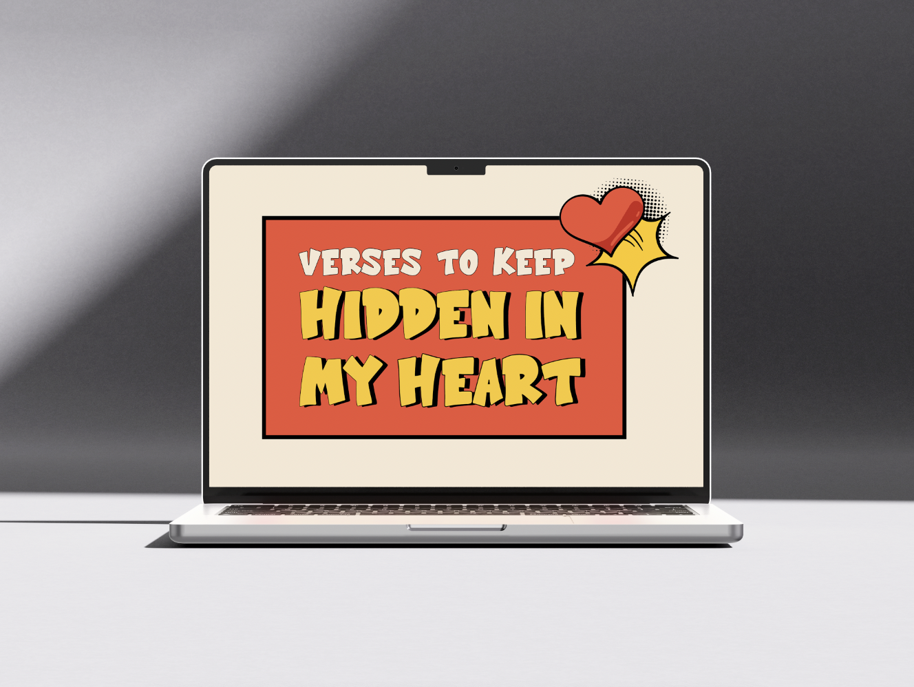 Laptop displaying a graphic with the text "Verses to Keep Hidden in My Heart" in bold yellow and white letters on a red background, with a cartoon red heart and a yellow starburst in the top right corner.