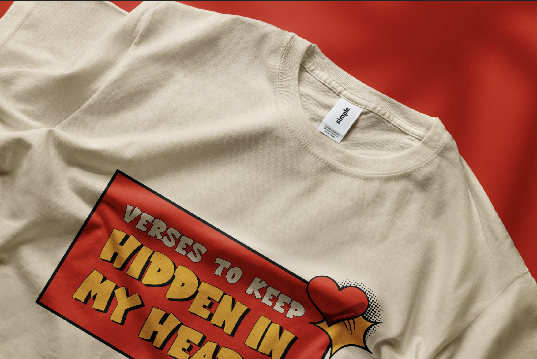 A beige T-shirt with a graphic design featuring red, yellow, and black text and a heart illustration, laid on a red background.