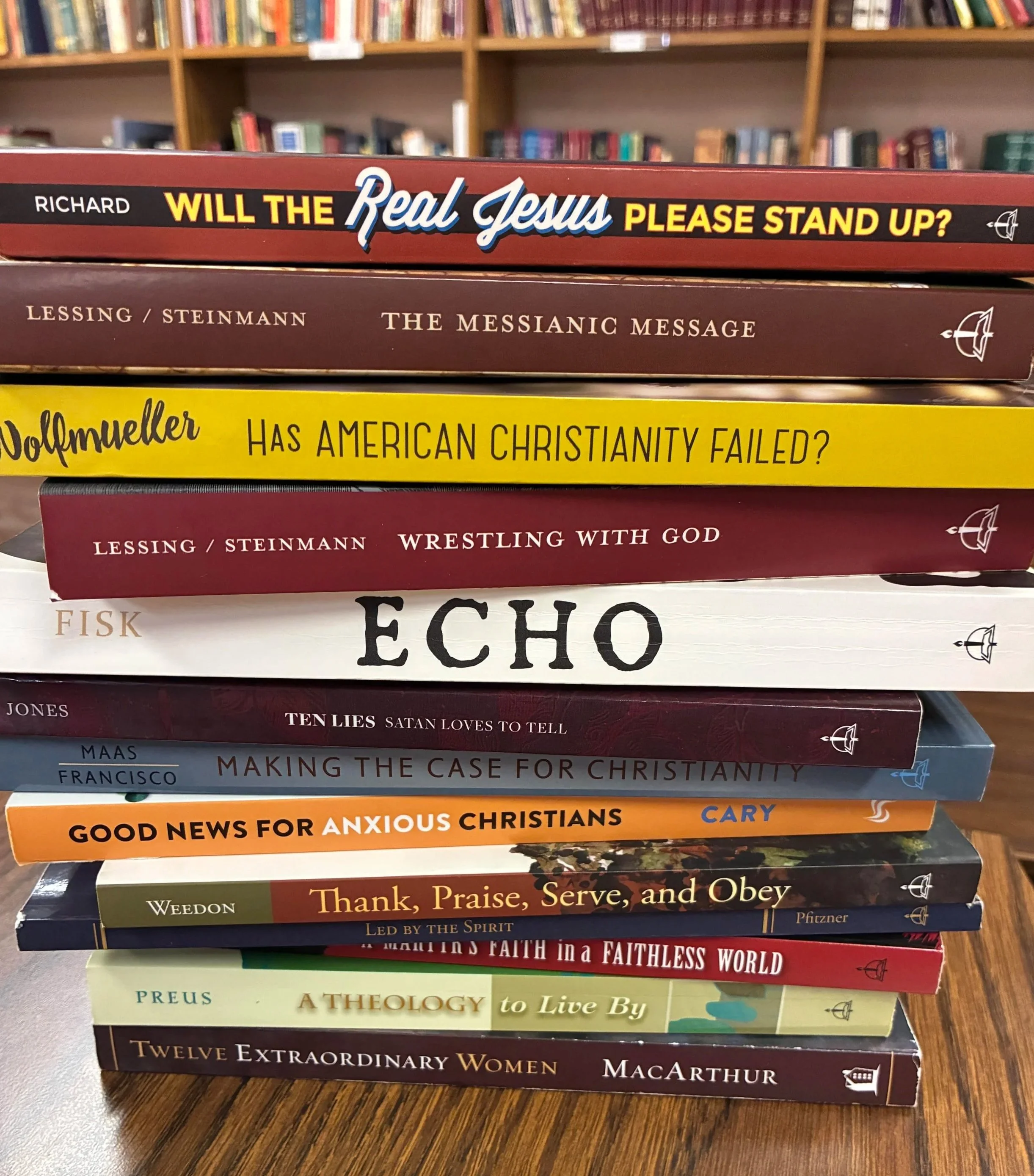 Stacked theology and Christian living books on a wooden table with a bookshelf in the background.