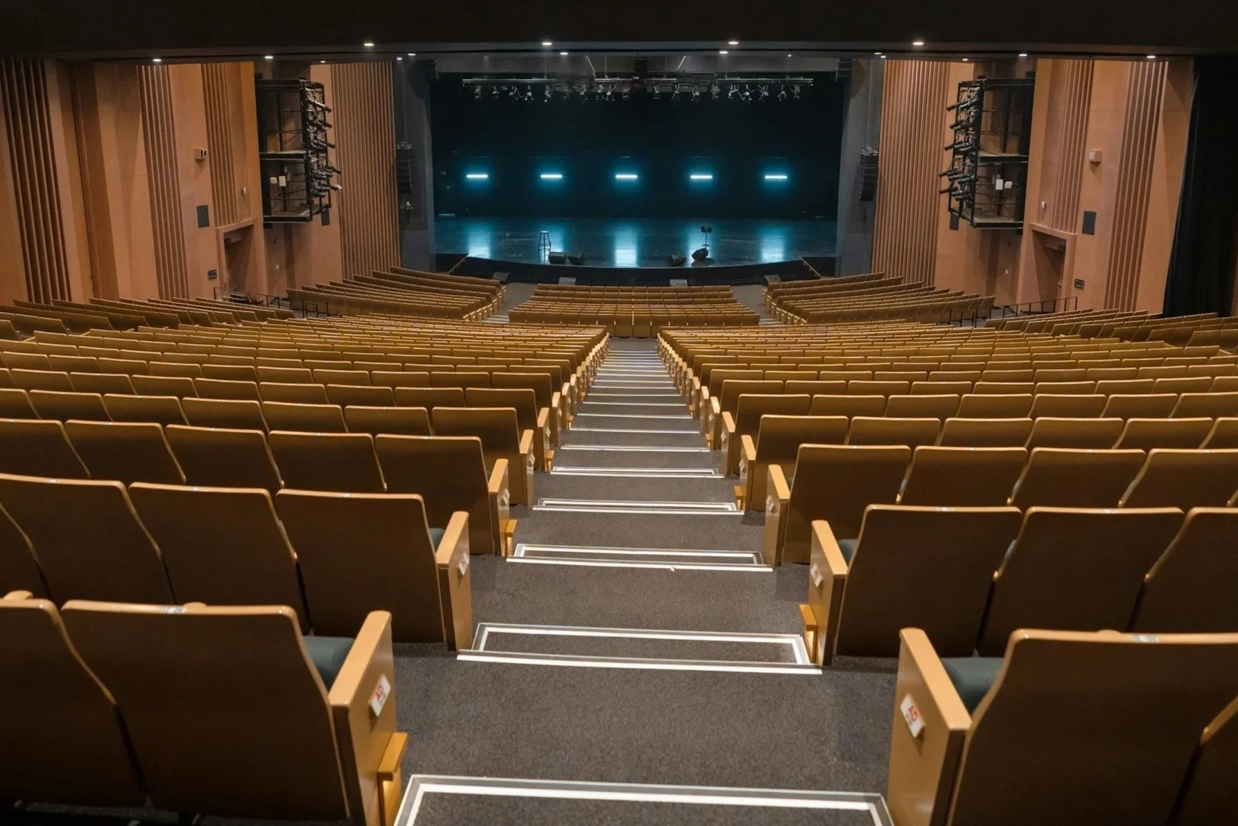 Empty theater with rows of brown seats, a stage with spotlights, and black walls with blue lights.