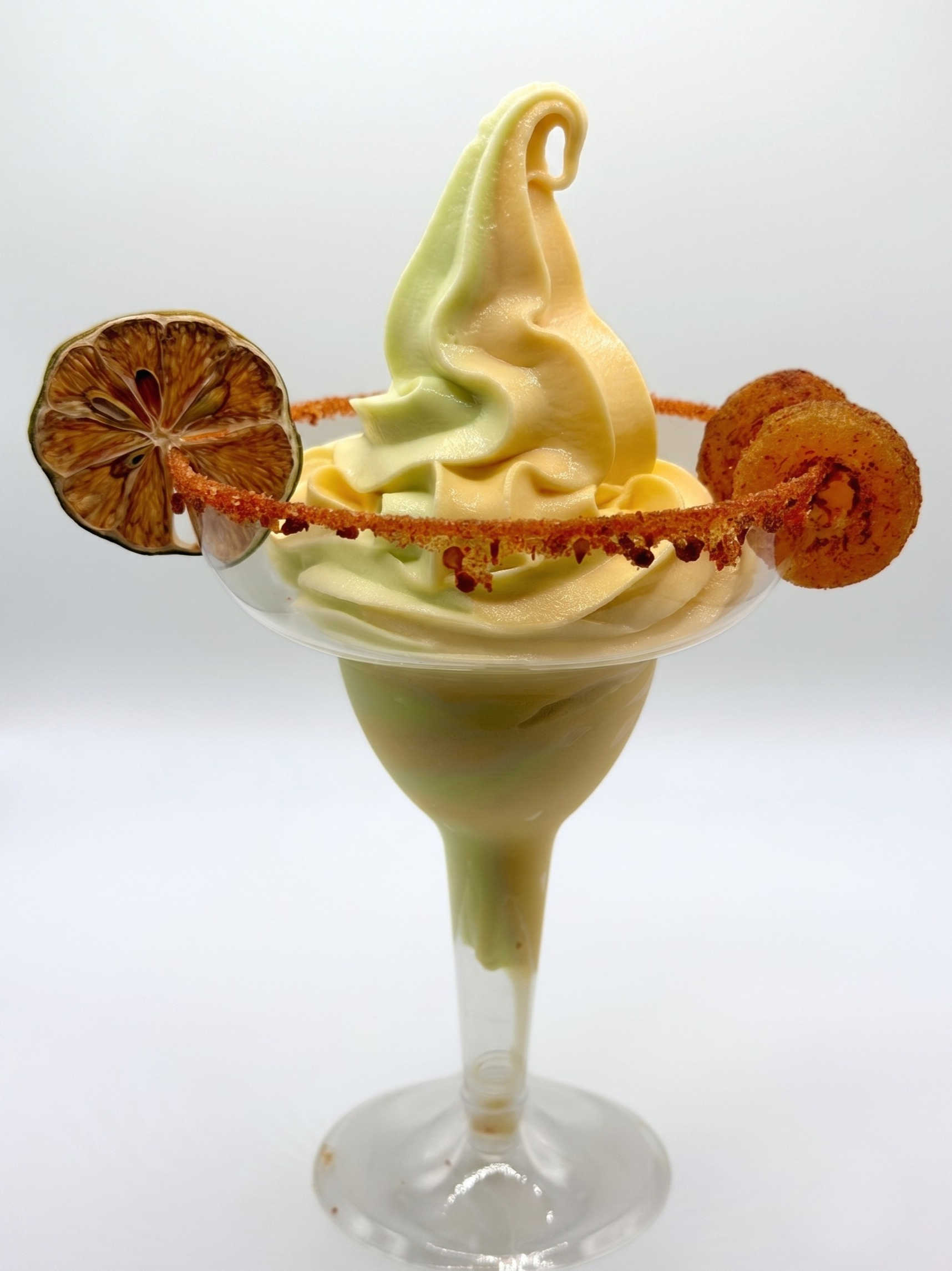 Lime and mango swirled soft-serve margarita in a margarita glass with a tajin rim and a dried lime slice garnish.