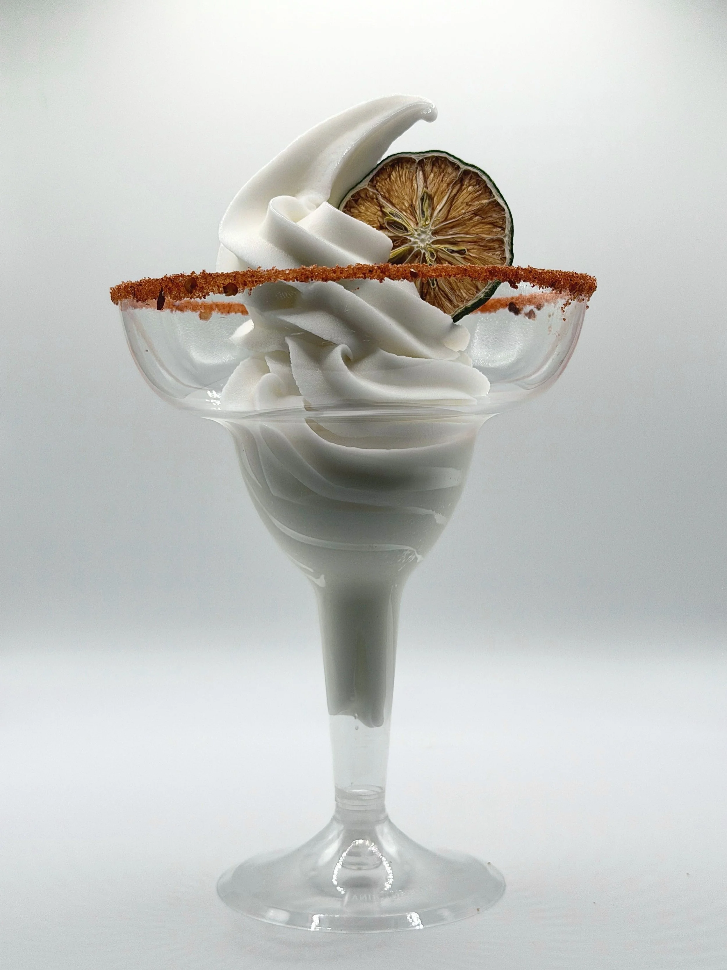 Coconut soft-serve margarita in a margarita glass with a tajin rim and a dried lime slice garnish.