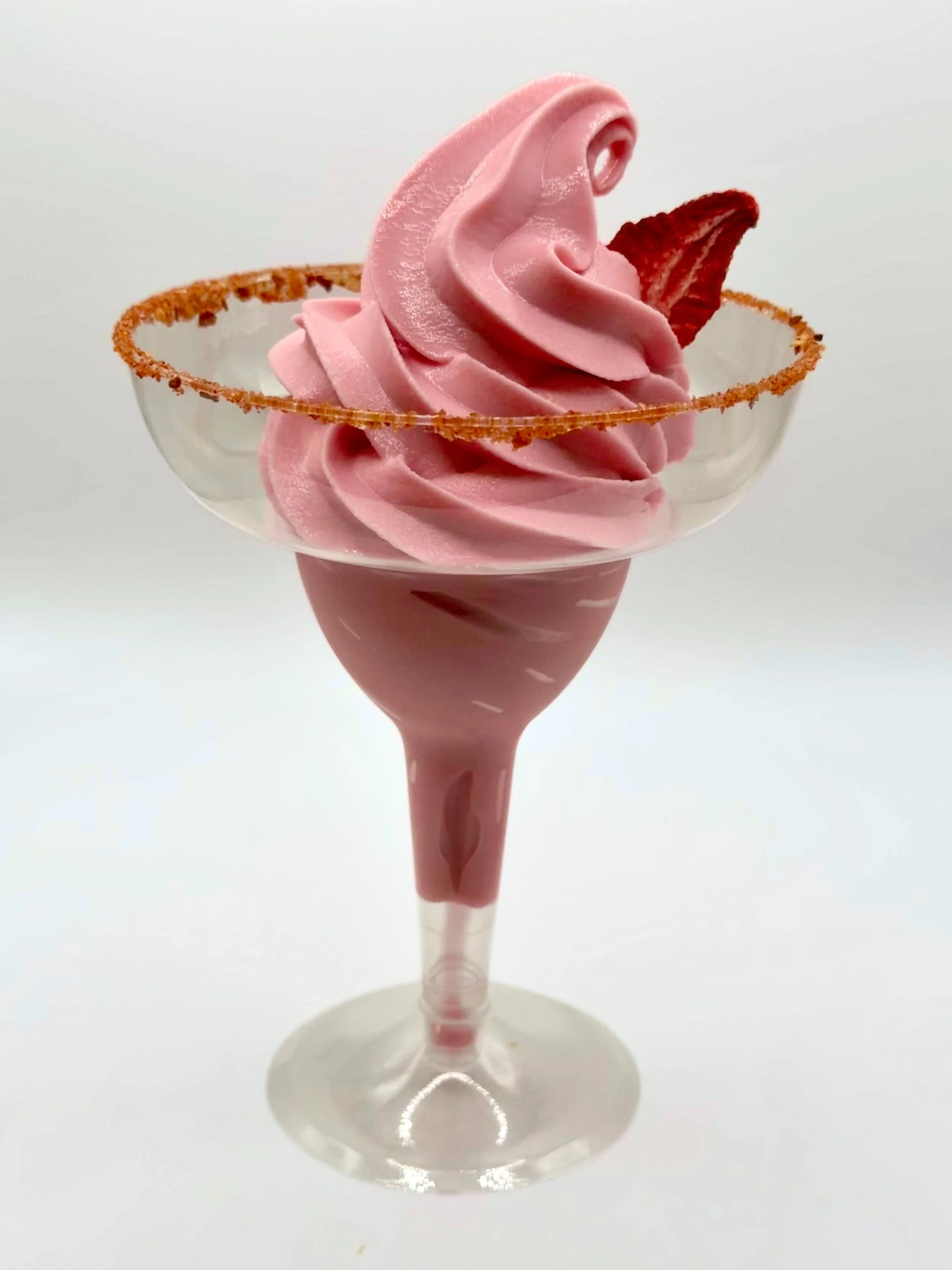 Strawberry soft-serve margarita in a margarita glass with a tajin rim and a dried strawberry slice garnish.