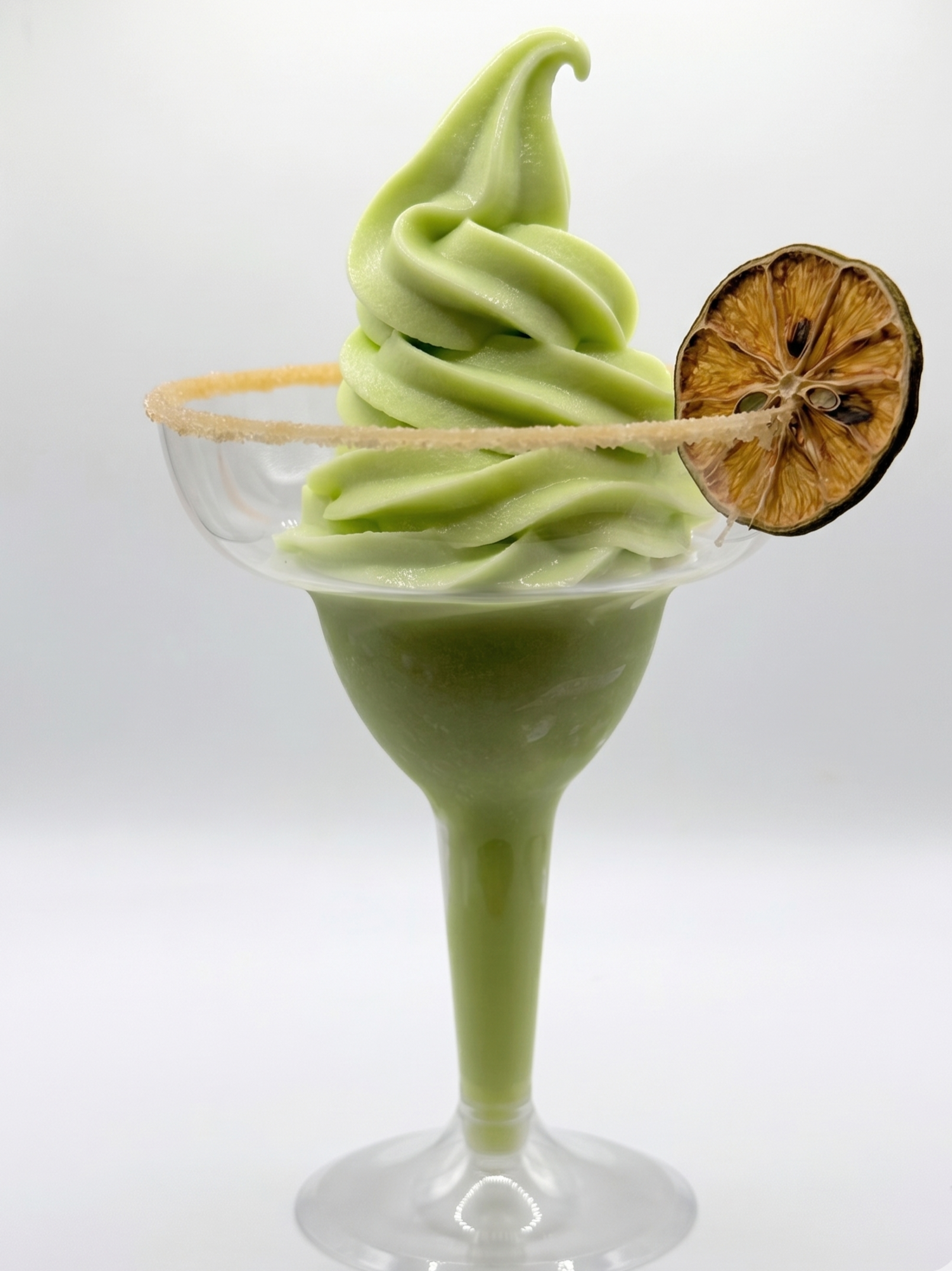 Lime soft serve margarita in a margarita glass garnished with a dried lime slice and a salted rim