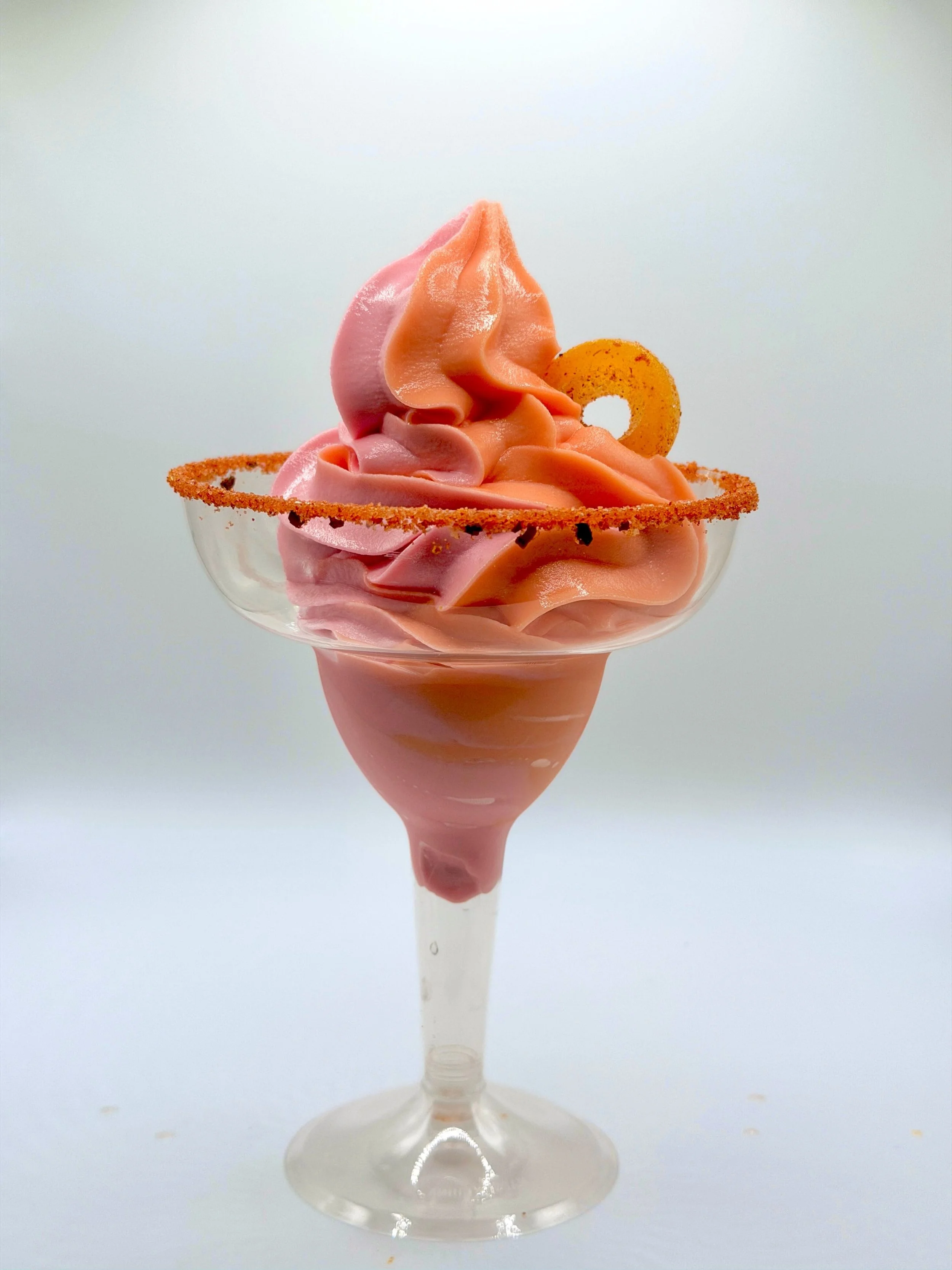 Strawberry and peach soft-serve margarita in a margarita glass with a tajin rim and a tajin candy ring garnish.
