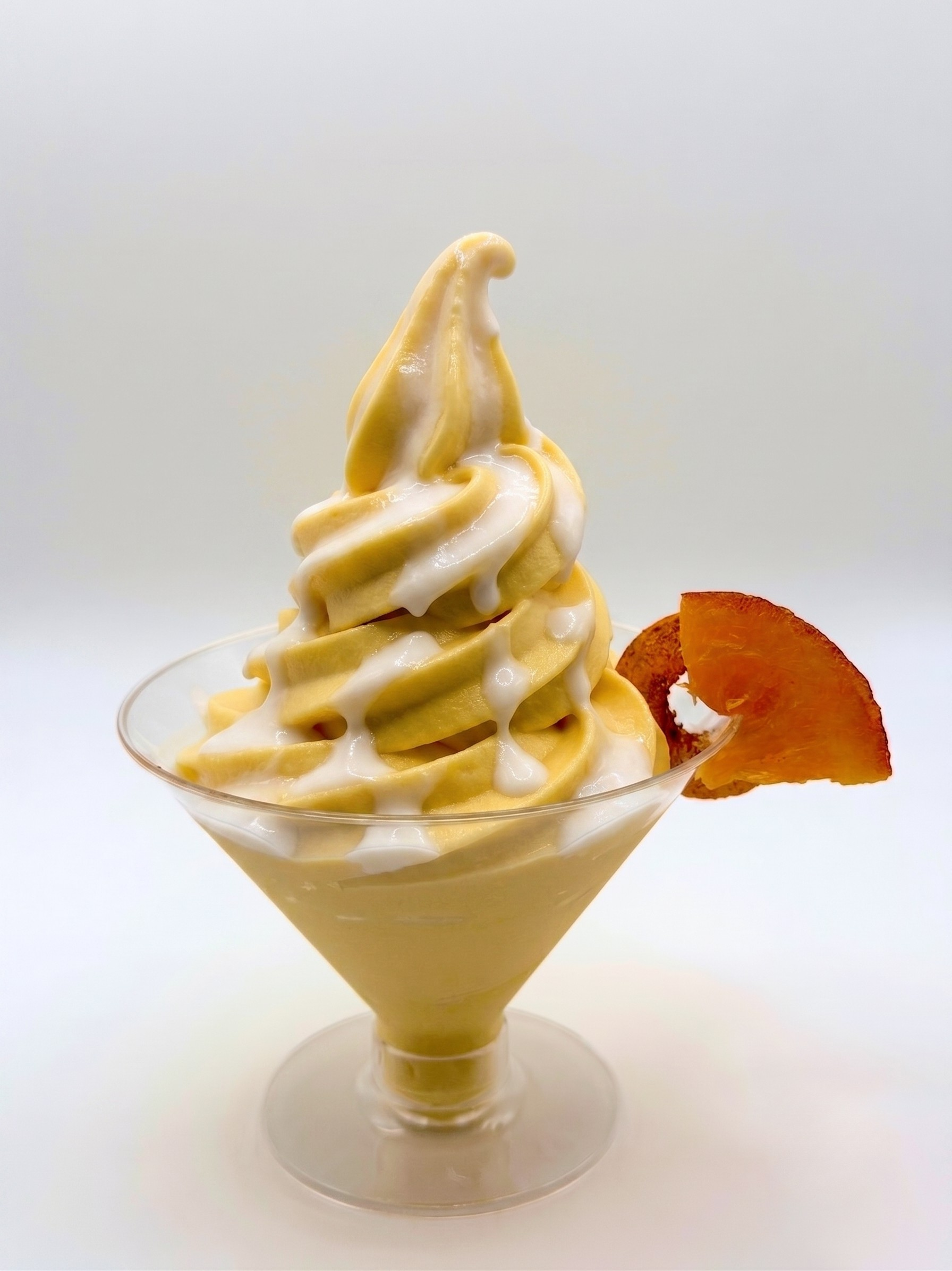 Soft serve orange dominican morir sonando cocktail with a drizzle of coconut cream sauce, garnished with a slice of dried orange, served in a martini glass.