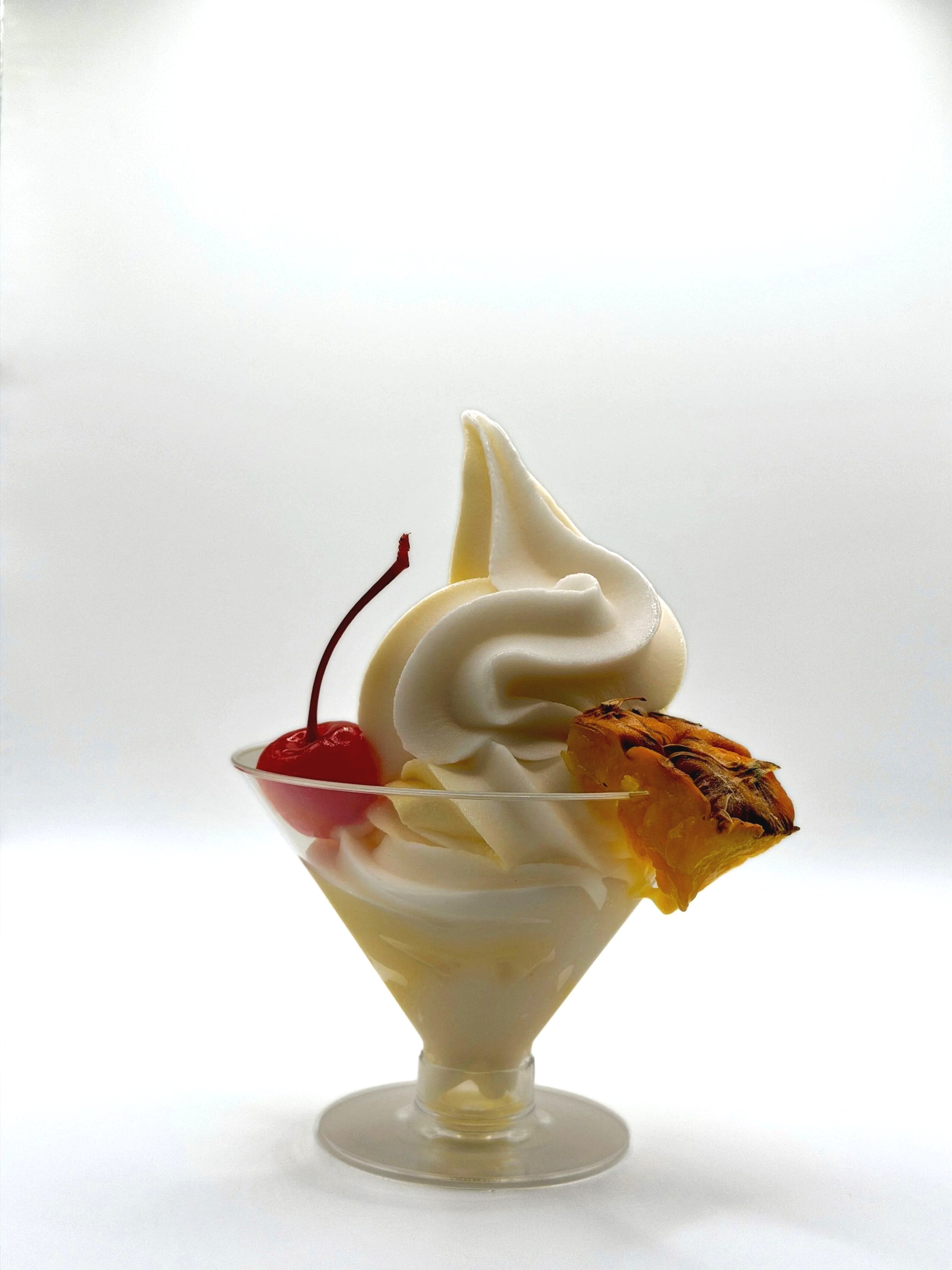 Creamy coconut and pineapple pina colada topped with a cherry, pineapple slice, and a piece of pineapple in a clear glass sundae dish against a white background.