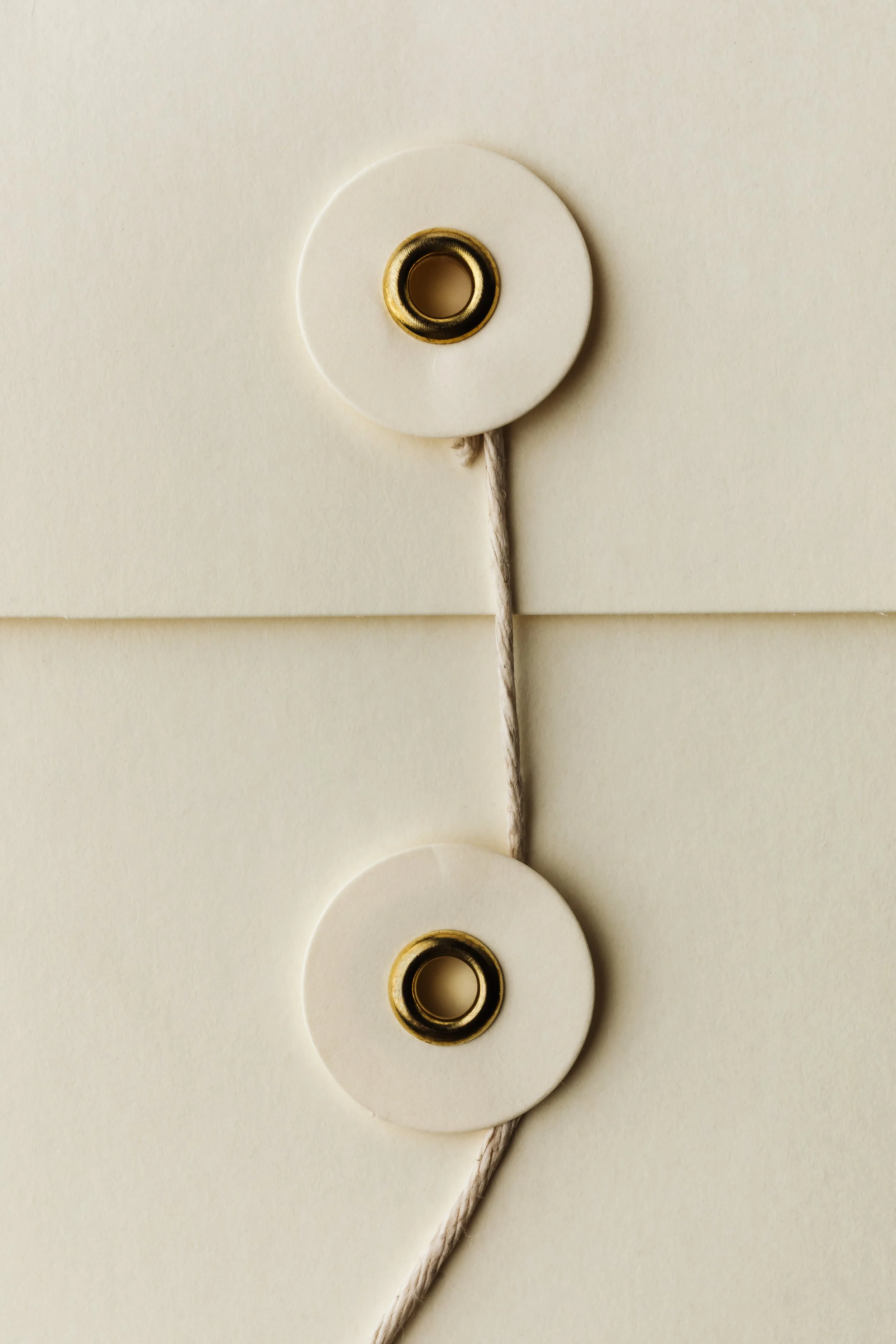 Close-up of string with two brass eyelets and circular white paper discs on a light background.