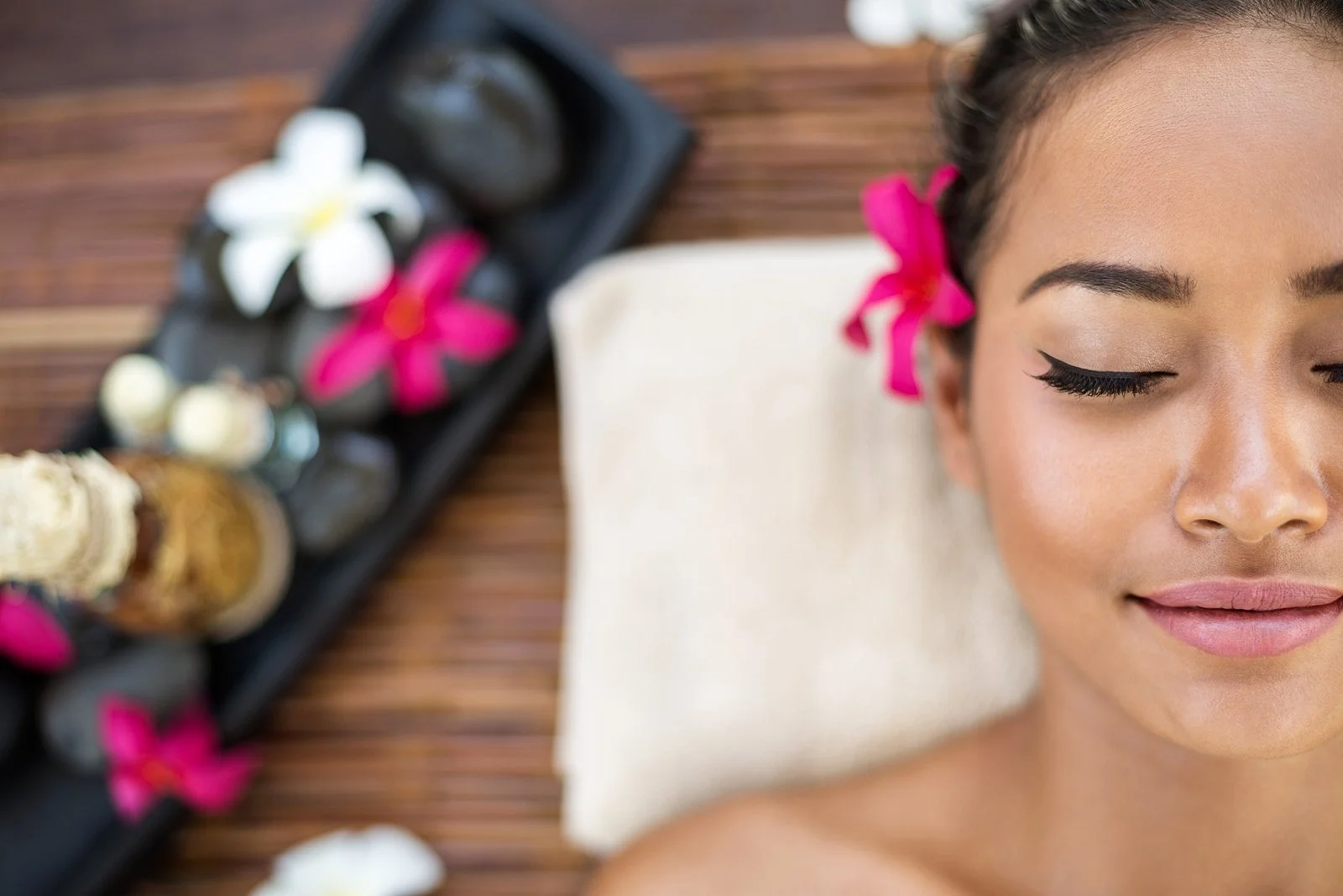 A woman with closed eyes receiving a massage, surrounded by flowers and spa products, in a relaxing setting.
