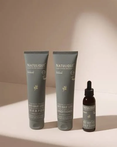 Three NATULIQUE hair treatment products including two tubes of shampoo and conditioner, and a small dropper bottle of scalp serum, placed on a white surface.