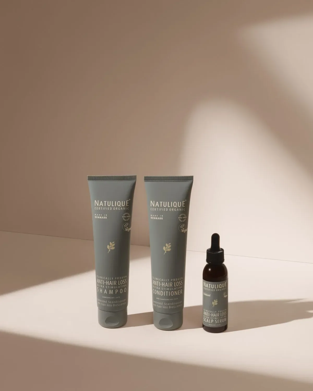 Three Natulique hair care products, shampoo, conditioner, and scalp serum, arranged on a surface with a plain background.