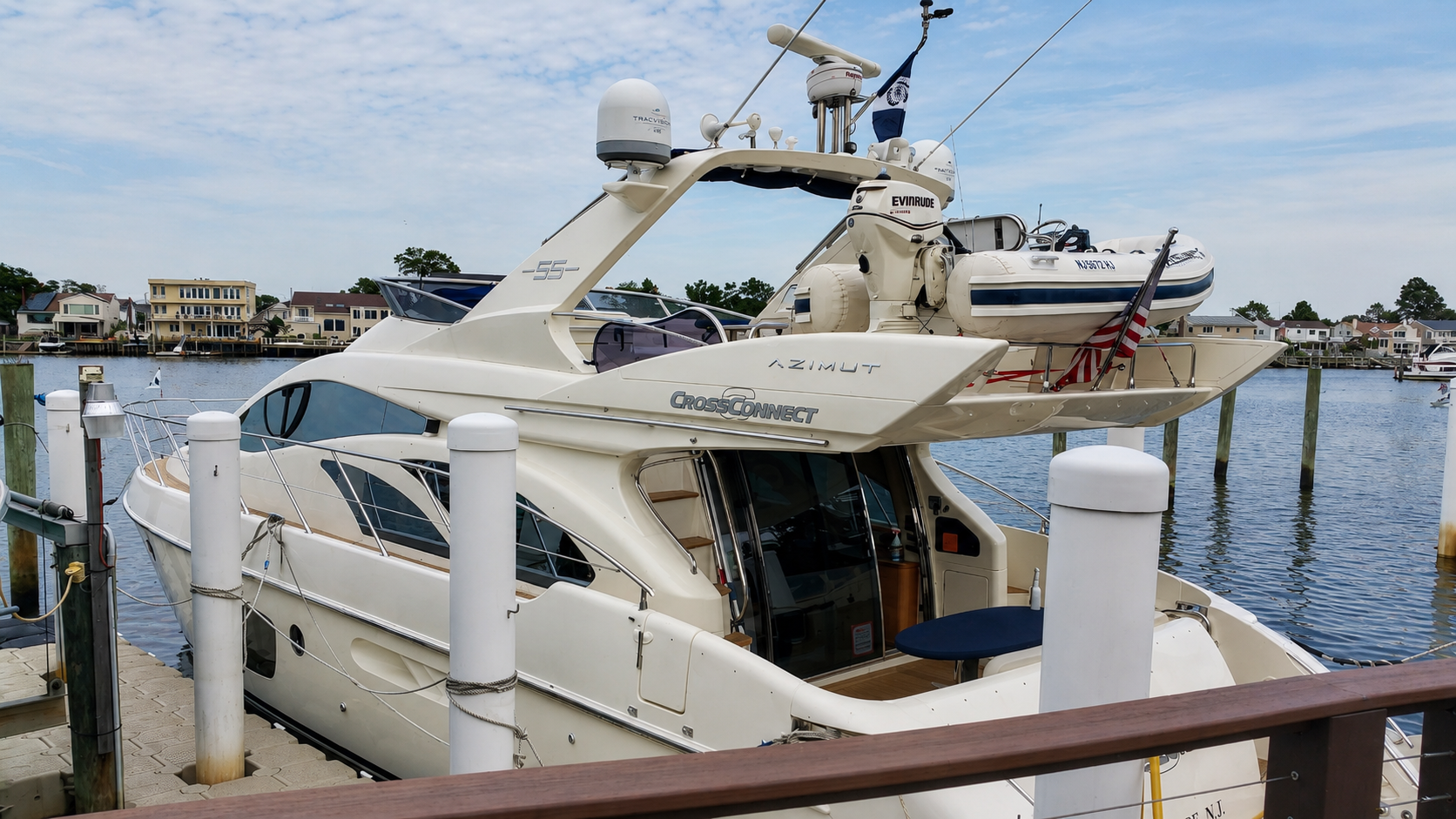 A white yacht named 'CrossConnect' docked at a marina, with houses and trees across the water and a partly cloudy sky overhead.