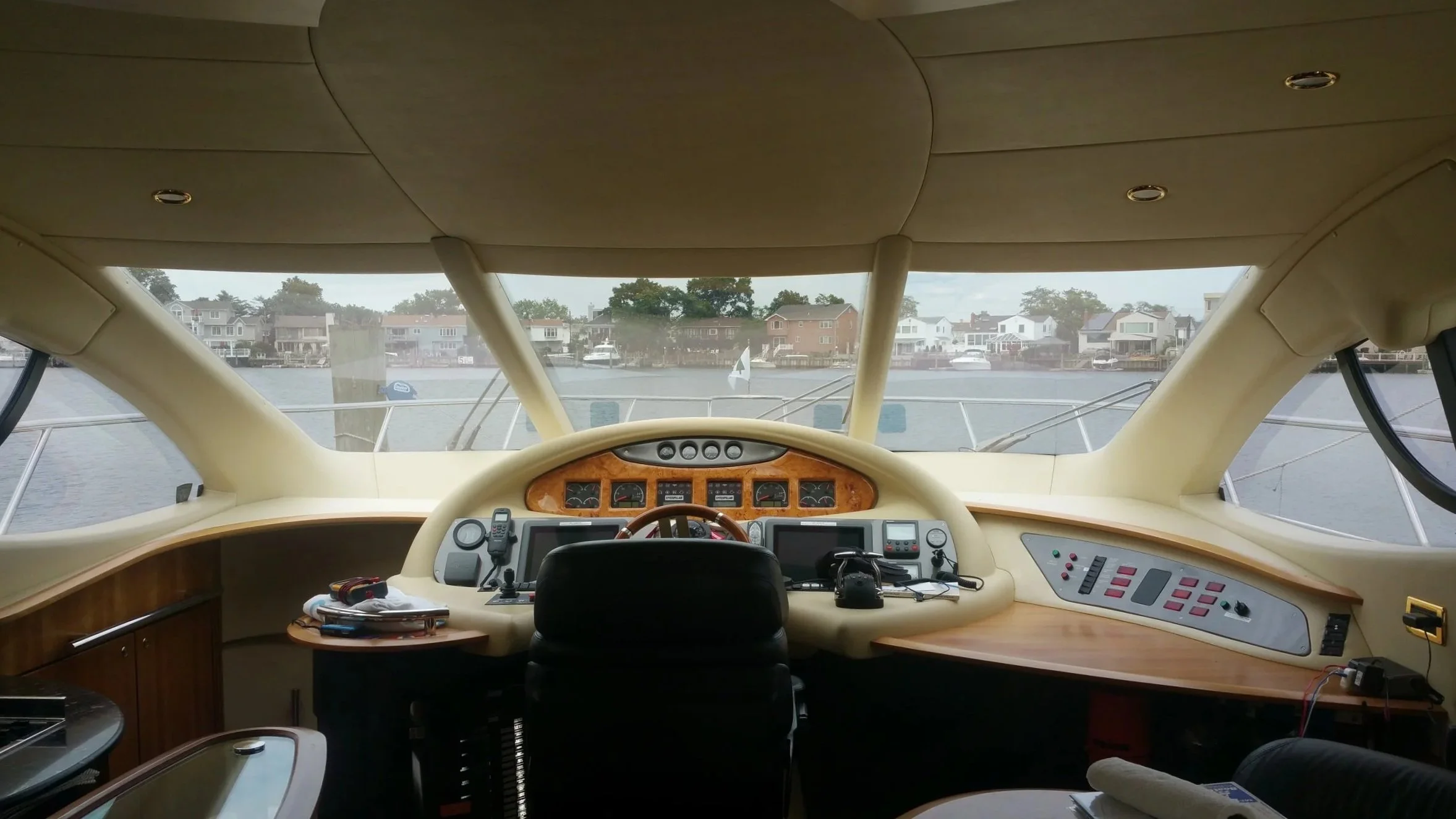 Interior view of a boat or yacht cockpit with a large windshield showing houses and a marina across the water.