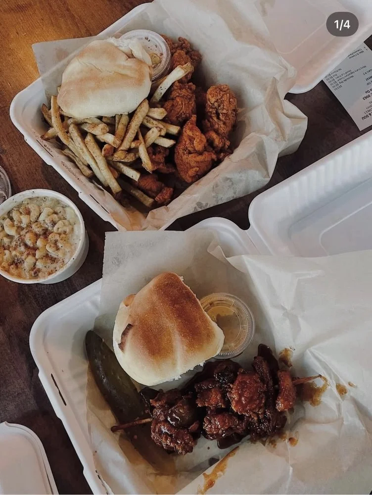 Two takeout containers with fried chicken, French fries, bread roll, pickle, and dipping sauces, along with a bowl of macaroni and cheese.