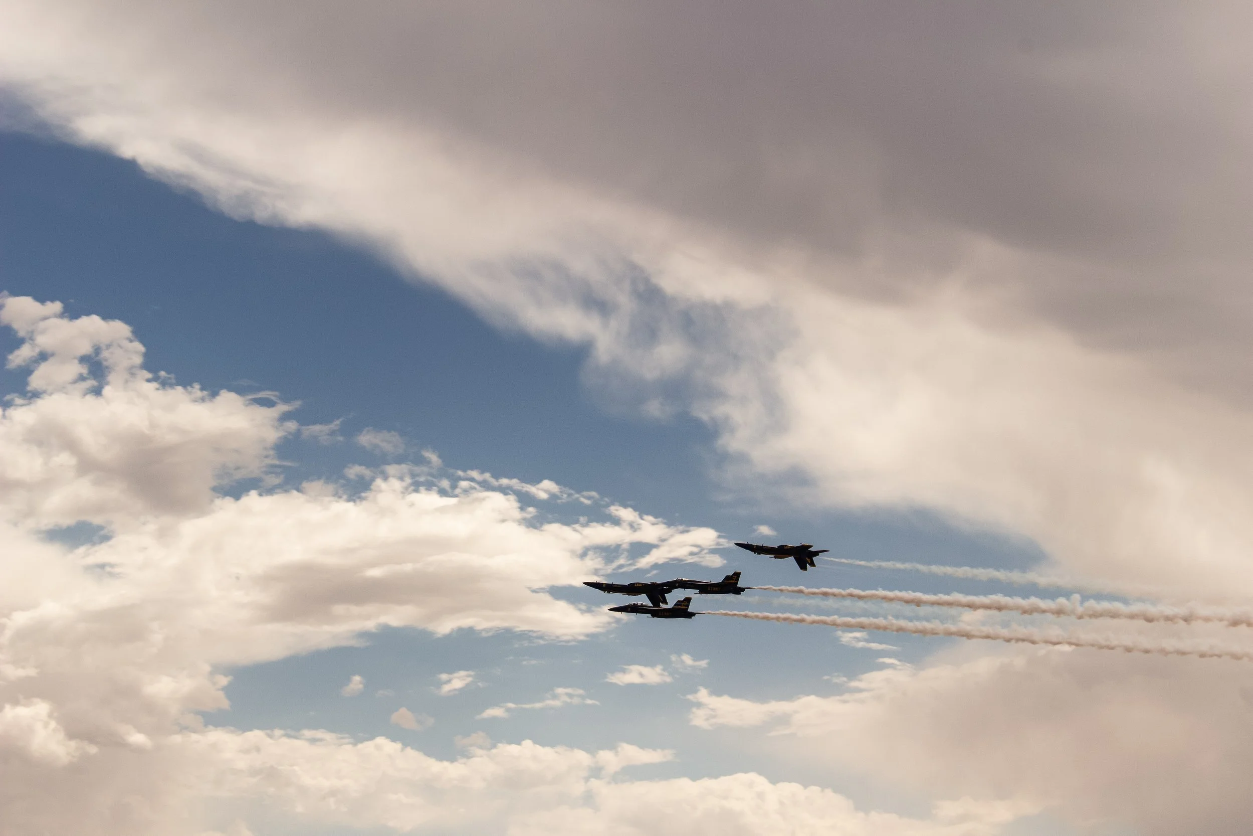 Three military jets flying in formation through a cloudy sky, leaving vapor trails behind them.