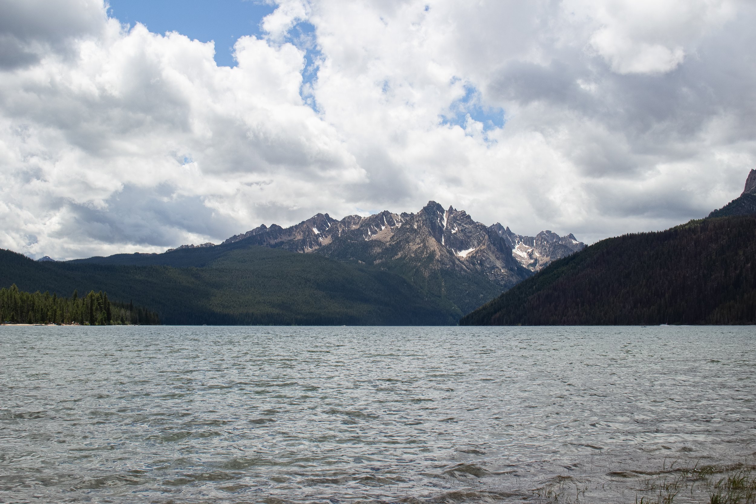 A large body of water with a mountain range in the background and a sky filled with clouds.