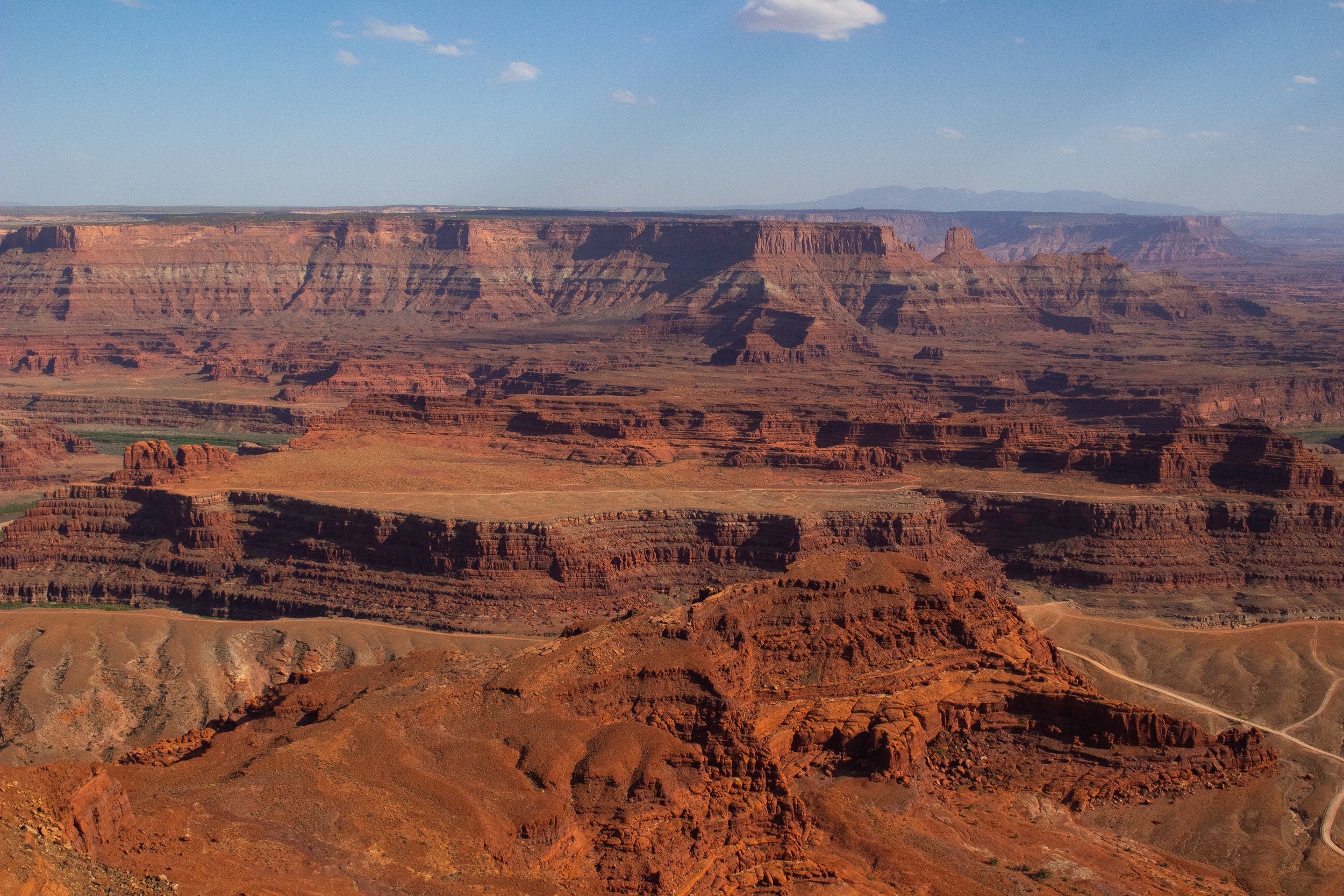 View of the Grand Canyon with layered red rocks and cliffs under a blue sky with a few small clouds.