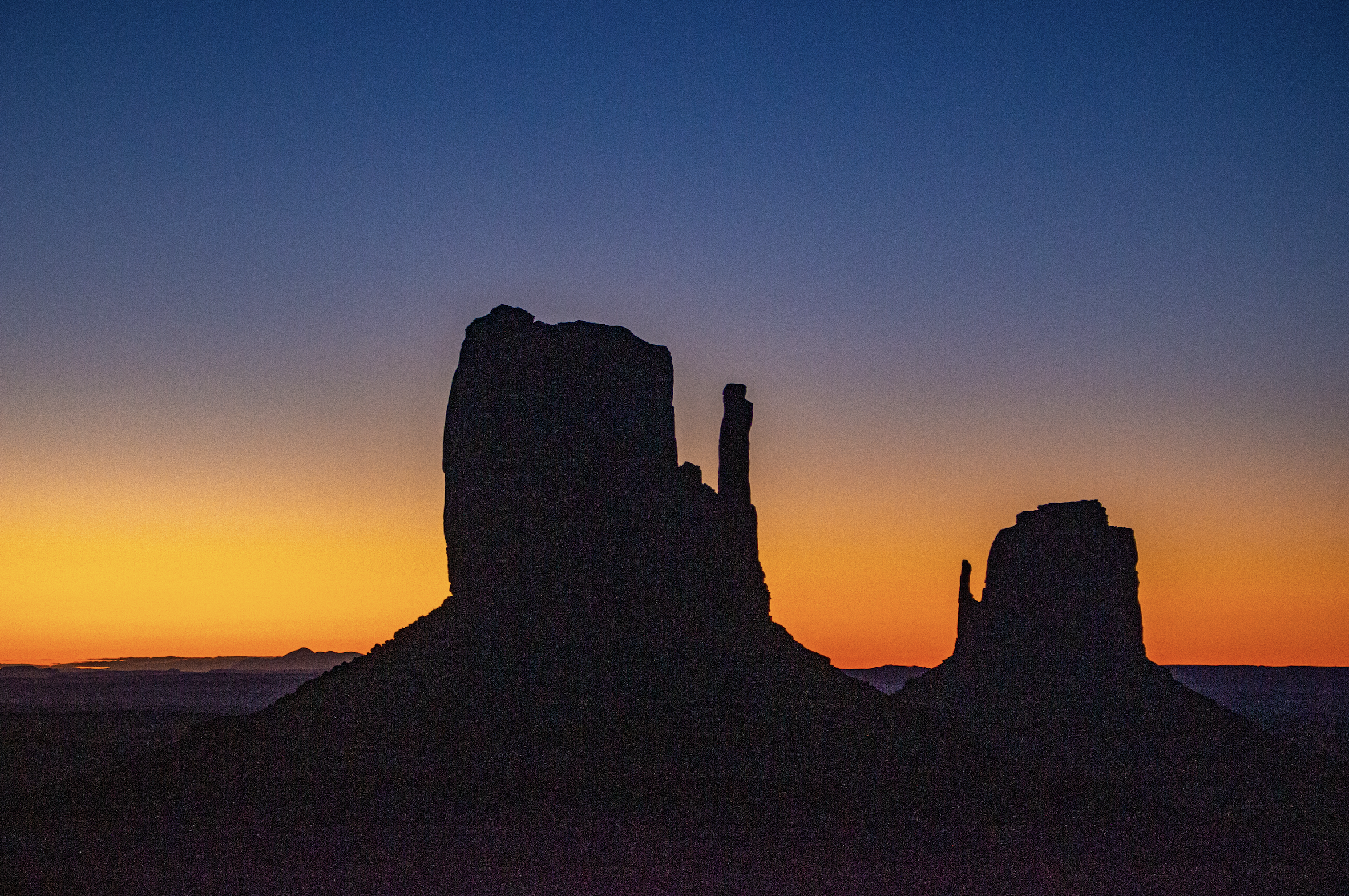Silhouettes of rock formations at sunset with a colorful gradient sky from orange to deep blue.