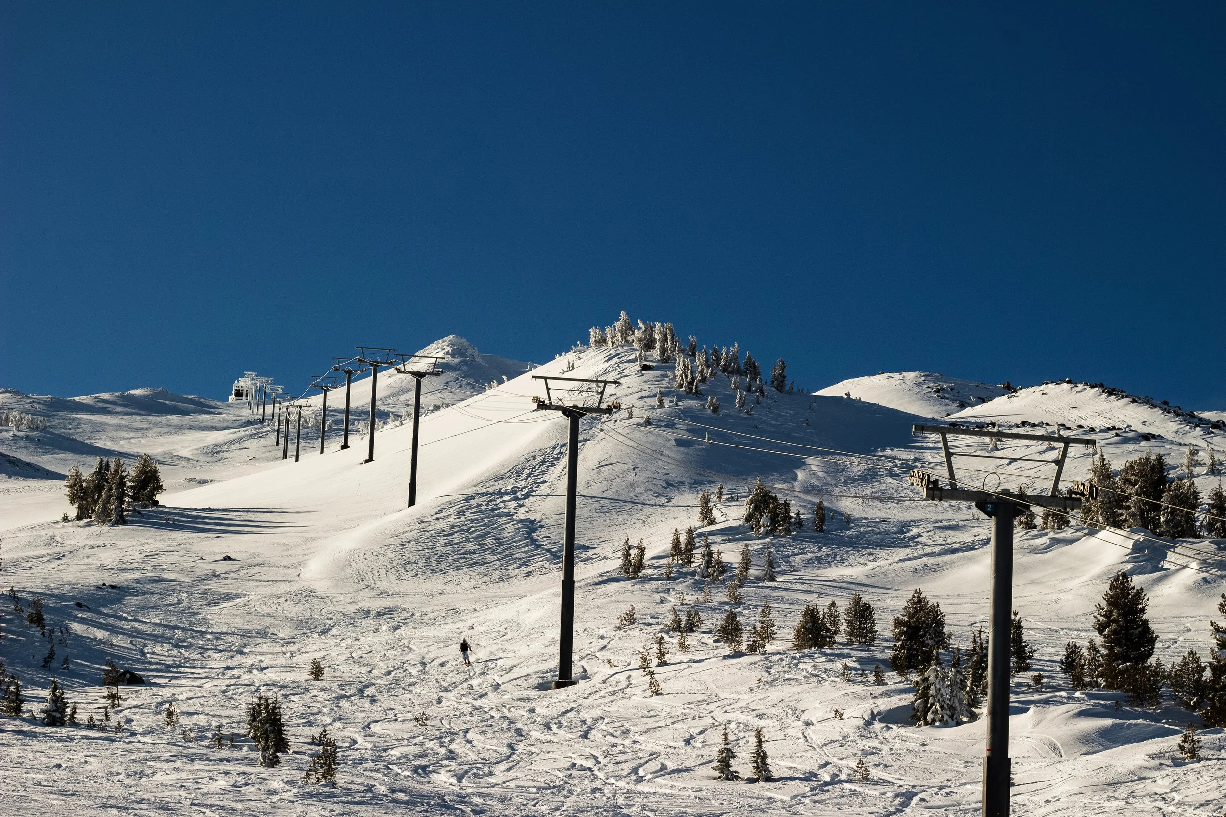 Snow-covered ski slopes with ski lifts and some trees under a clear blue sky.