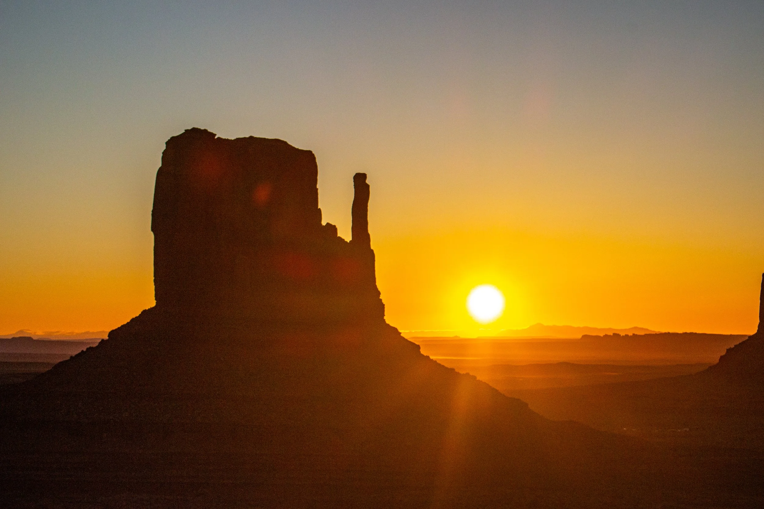 Silhouette of a rock formation at sunset with the sun near the horizon, creating a warm golden glow in the sky.