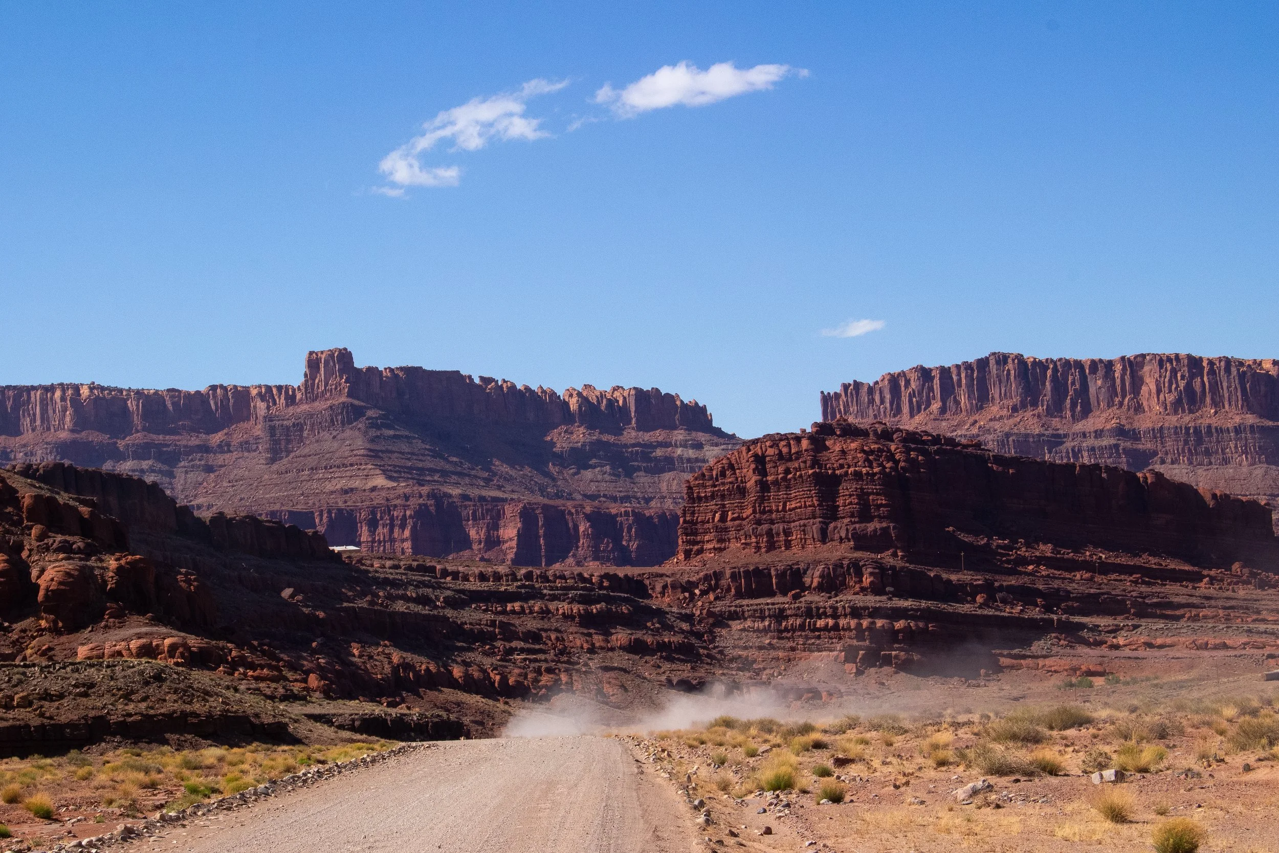 Dirt road leading into the Grand Canyon with red rock formations and a blue sky with a few white clouds.