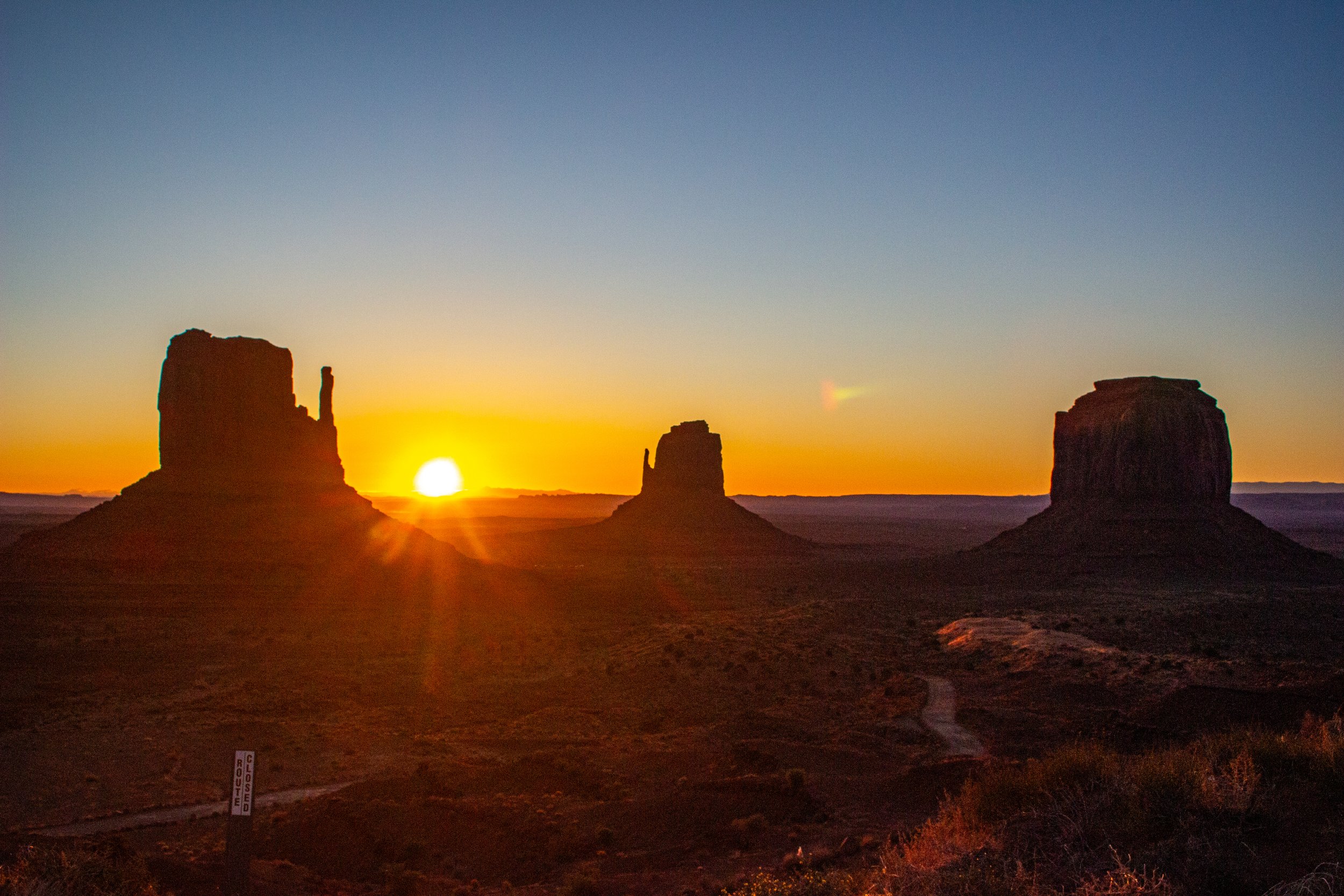 Sunset over the Monument Valley with three large buttes silhouetted against the colorful sky.
