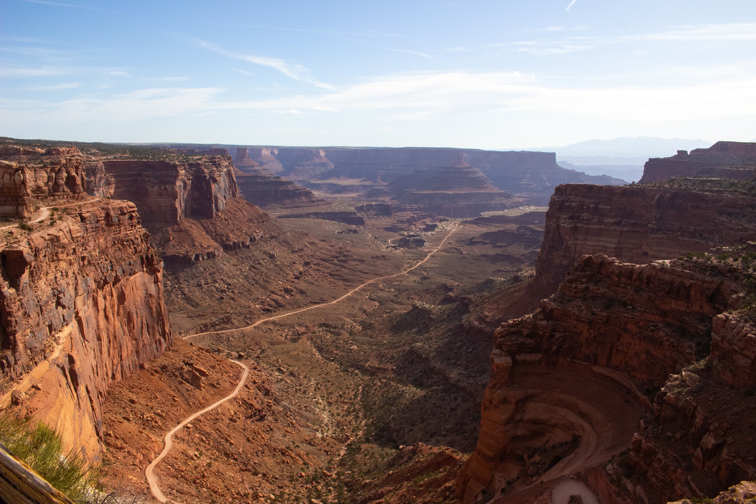View of the Grand Canyon showing layered rock formations, a dirt path, and a partly cloudy sky.