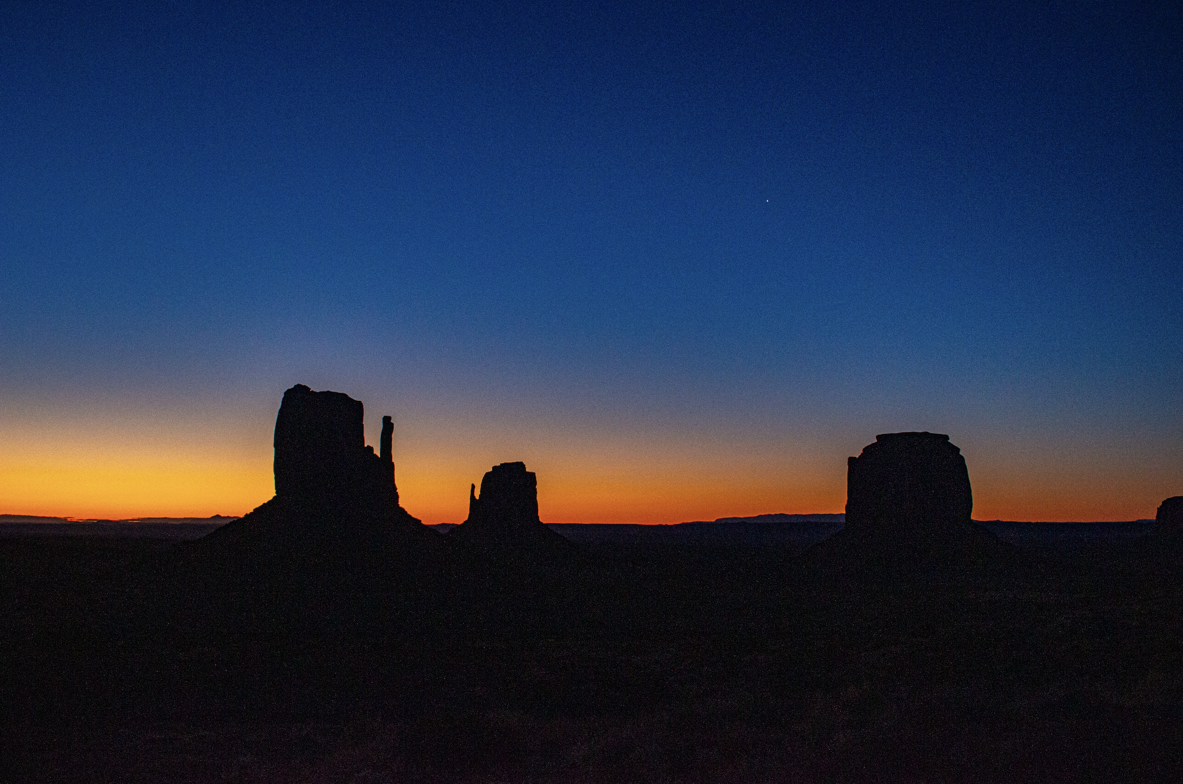 Silhouette of rock formations against a colorful sunset sky with a single bright star visible.
