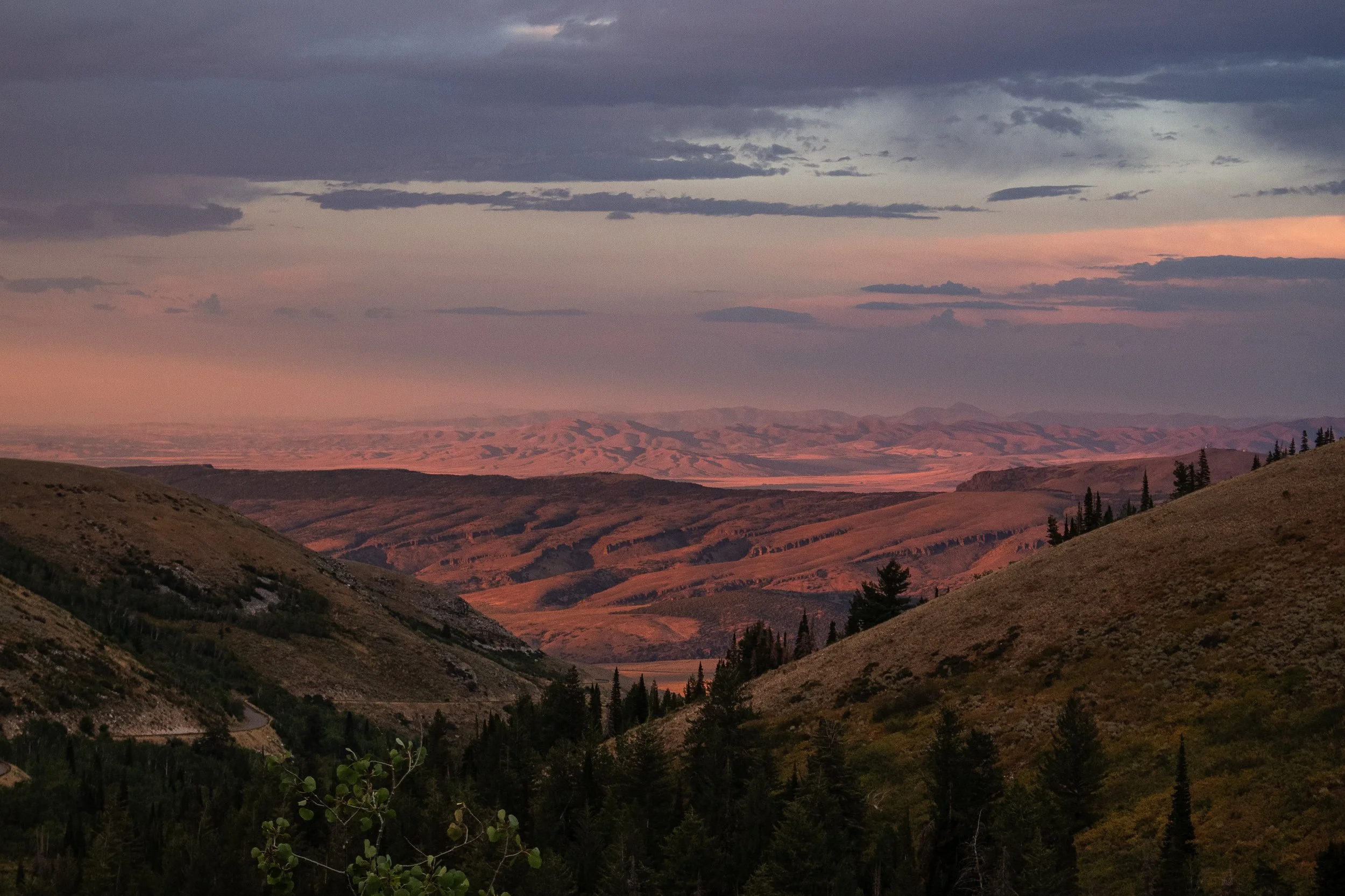 Scenic view of rolling hills and mountains at sunset with a colorful sky and scattered clouds.