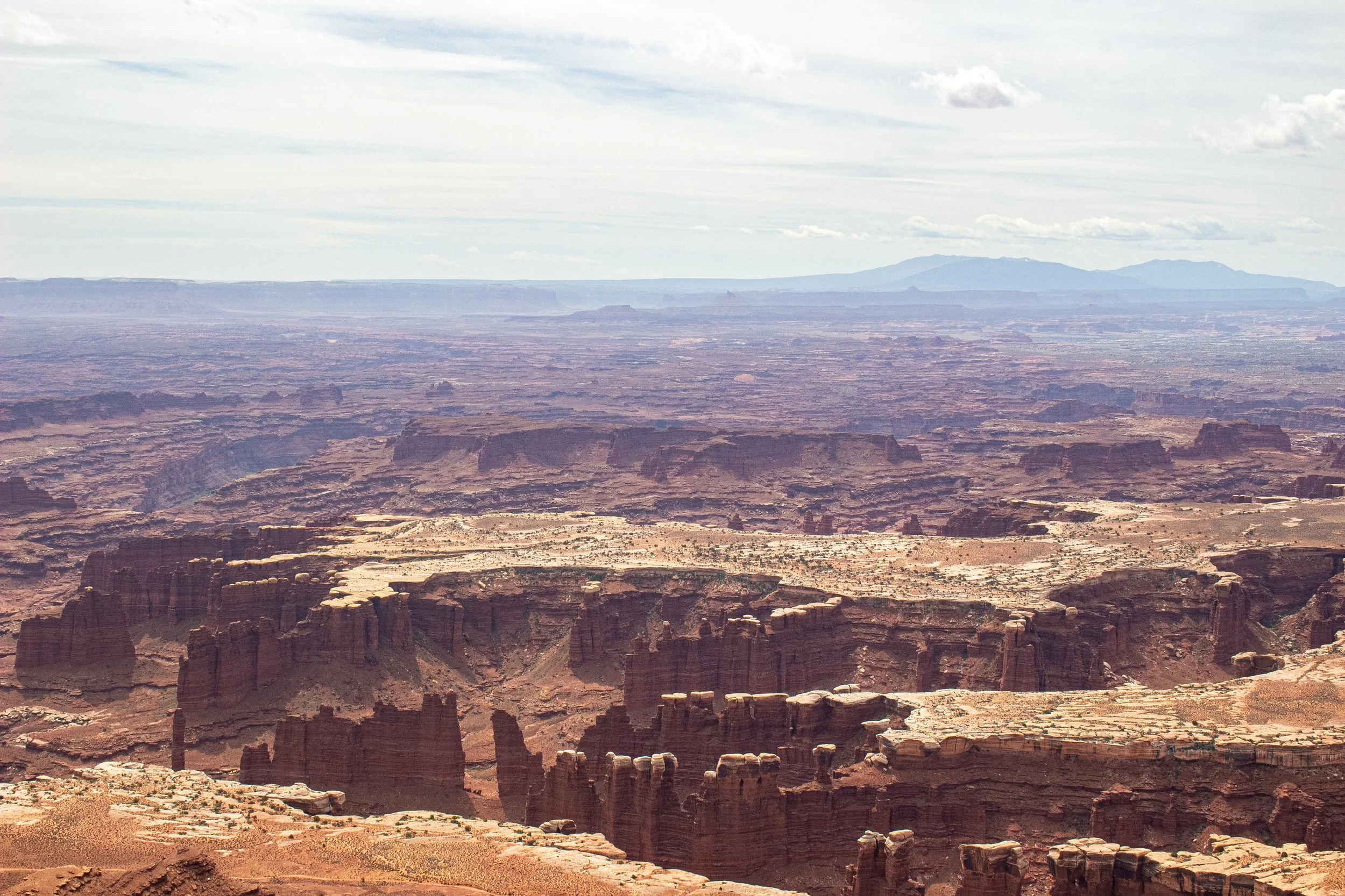 A vast canyon landscape with layered rock formations and rugged cliffs under a cloudy sky.