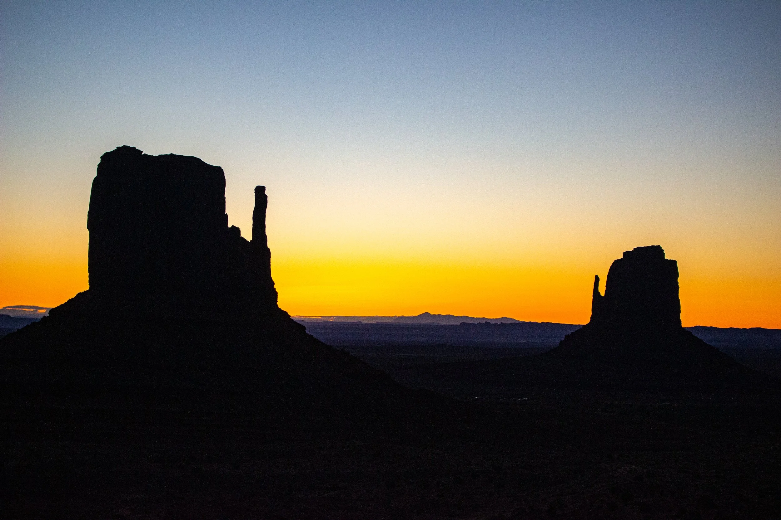 Silhouettes of rock formations against a colorful sunset sky in a desert landscape.