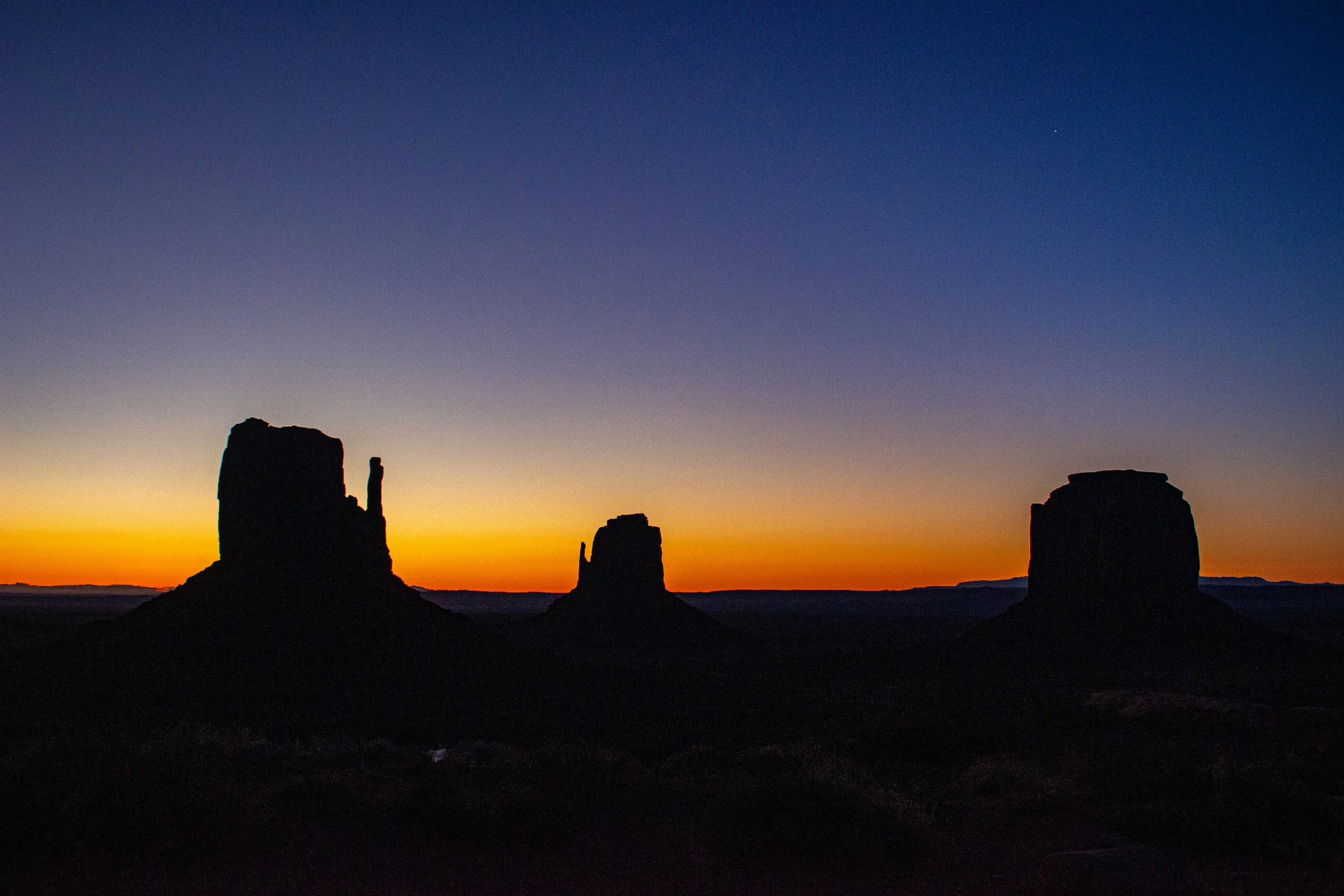 Silhouette of ancient rock formations against a colorful sunset sky with a star visible in the upper right.