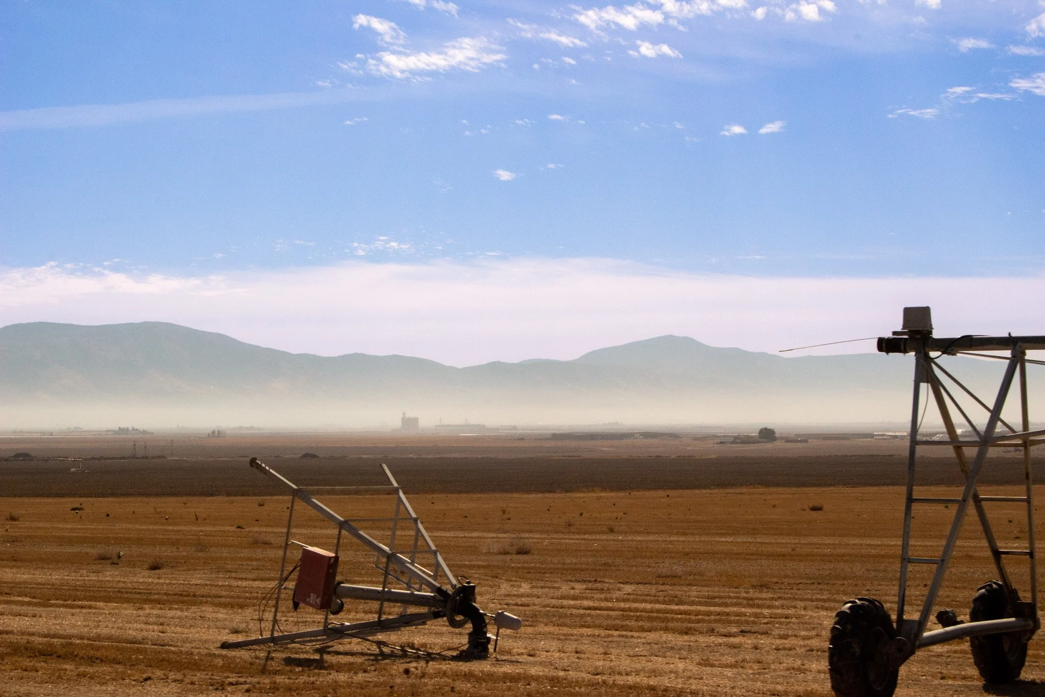 A wide open landscape with geological mountains in the background, and developing oil or gas drilling rigs in the foreground with equipment and machinery set up on dry, flat land.