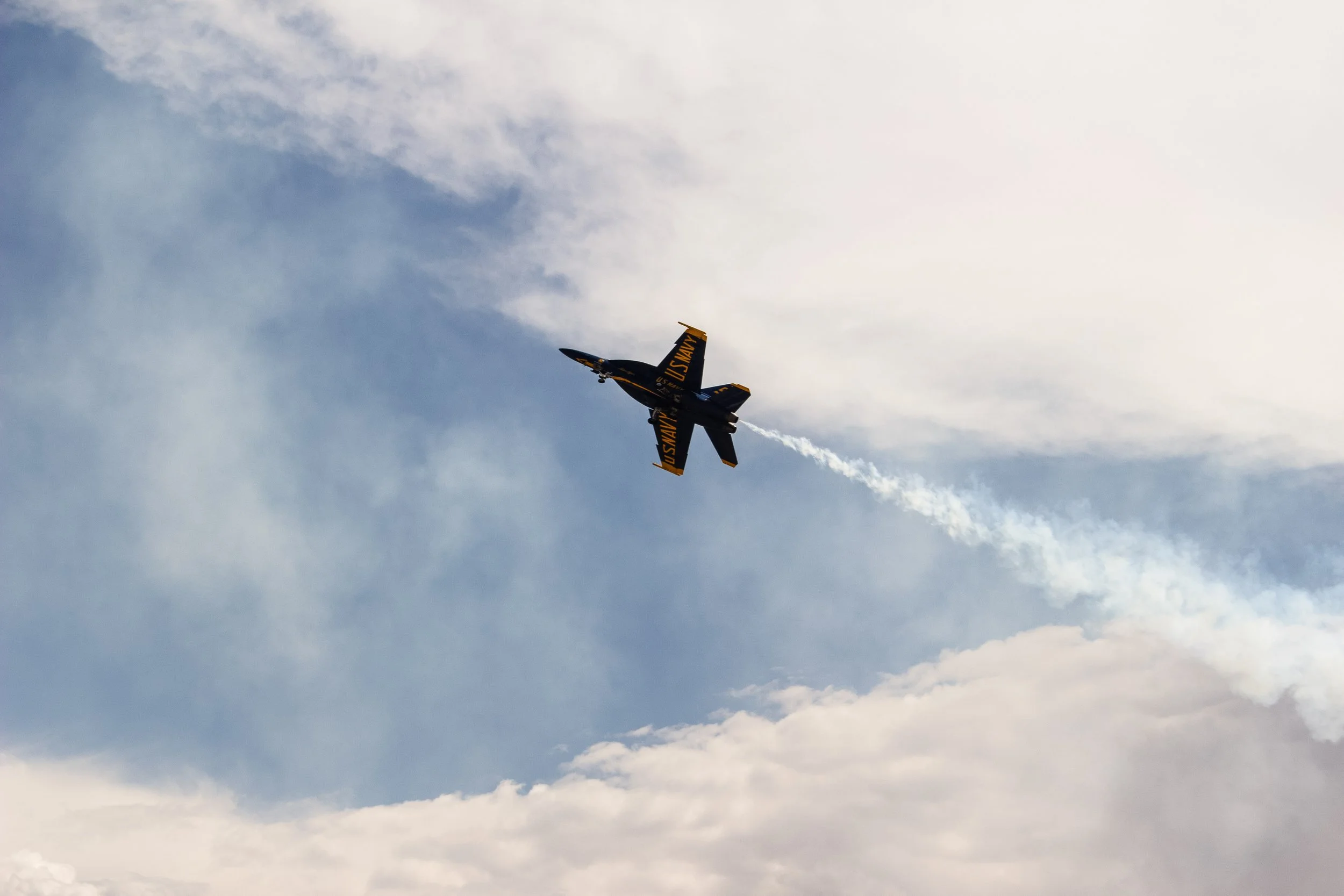 A fighter jet flying in the sky leaving a trail of white smoke behind, with clouds surrounding it.