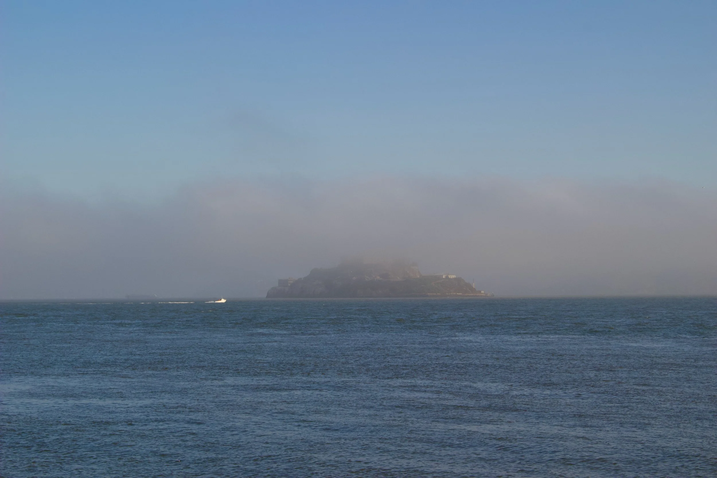 Ocean with a distant island and a boat on the water under a clear sky.