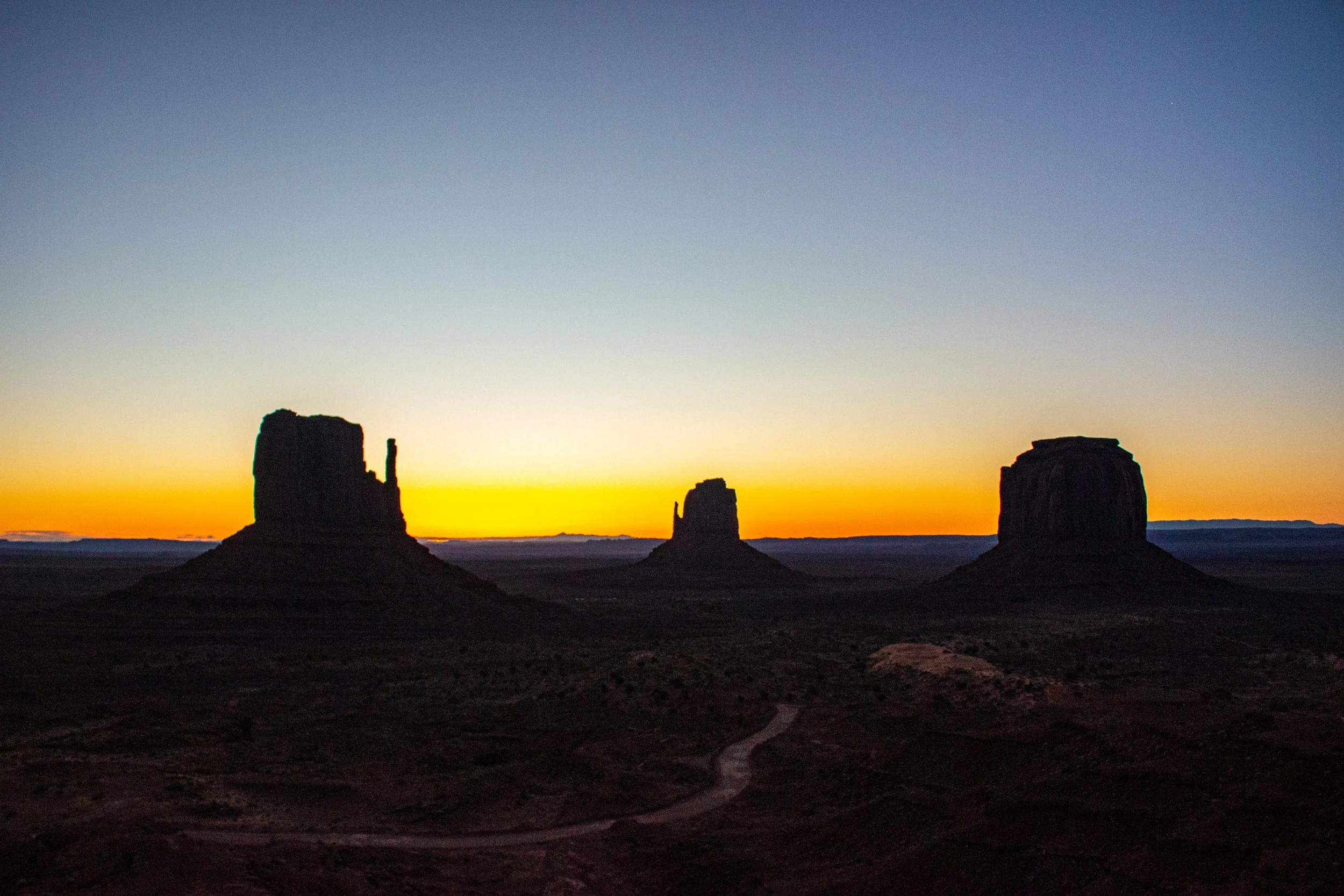 Silhouettes of three large rock formations in a desert landscape during sunset, with a colorful sky and a star visible.