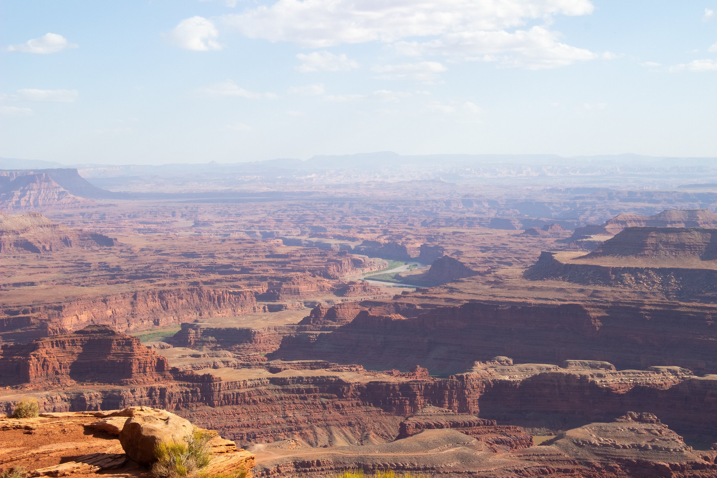 Scenic view of the Grand Canyon with layered rock formations, a river flowing at the bottom, and a partly cloudy sky above.