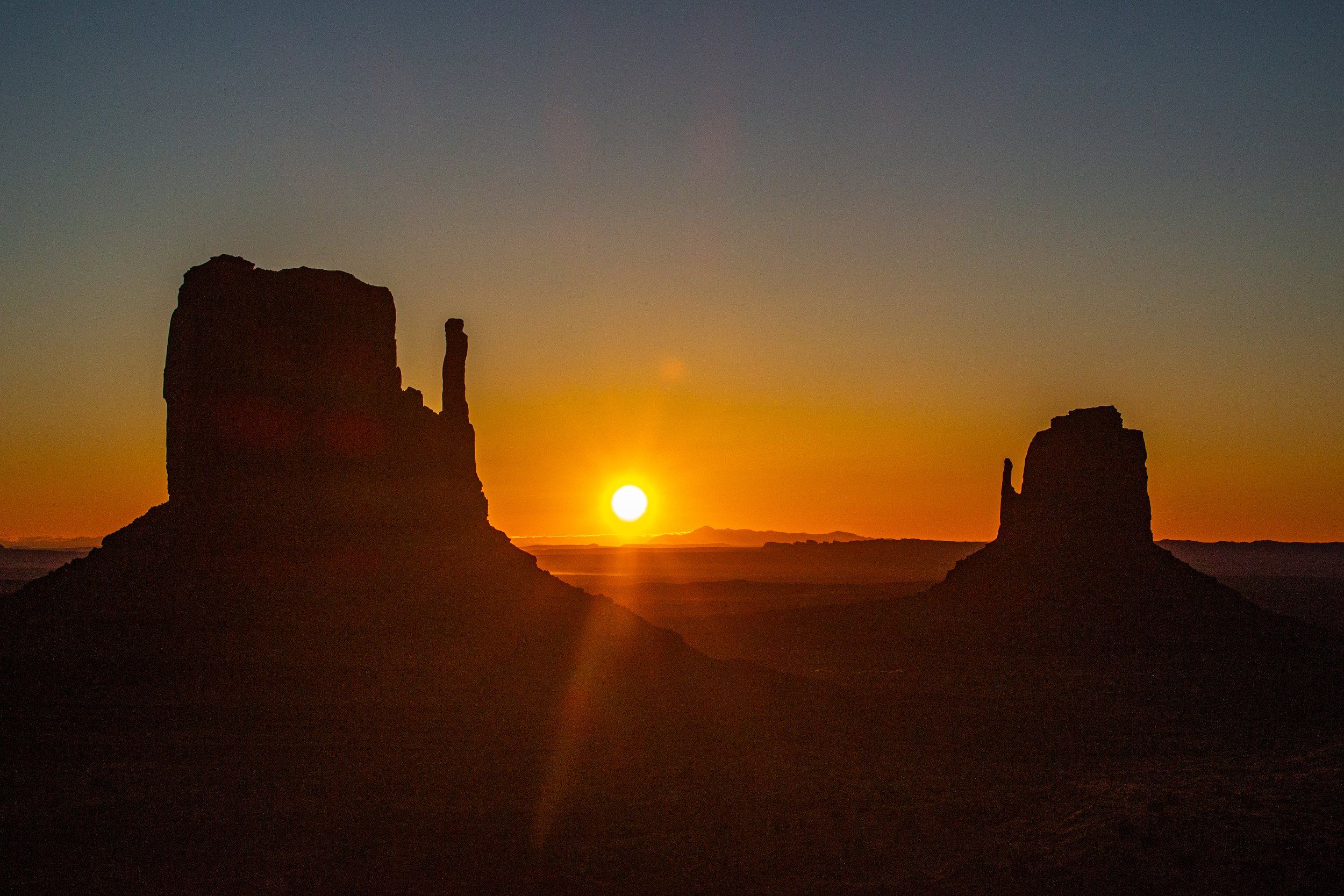 Sunset over desert with rock formations in silhouette.