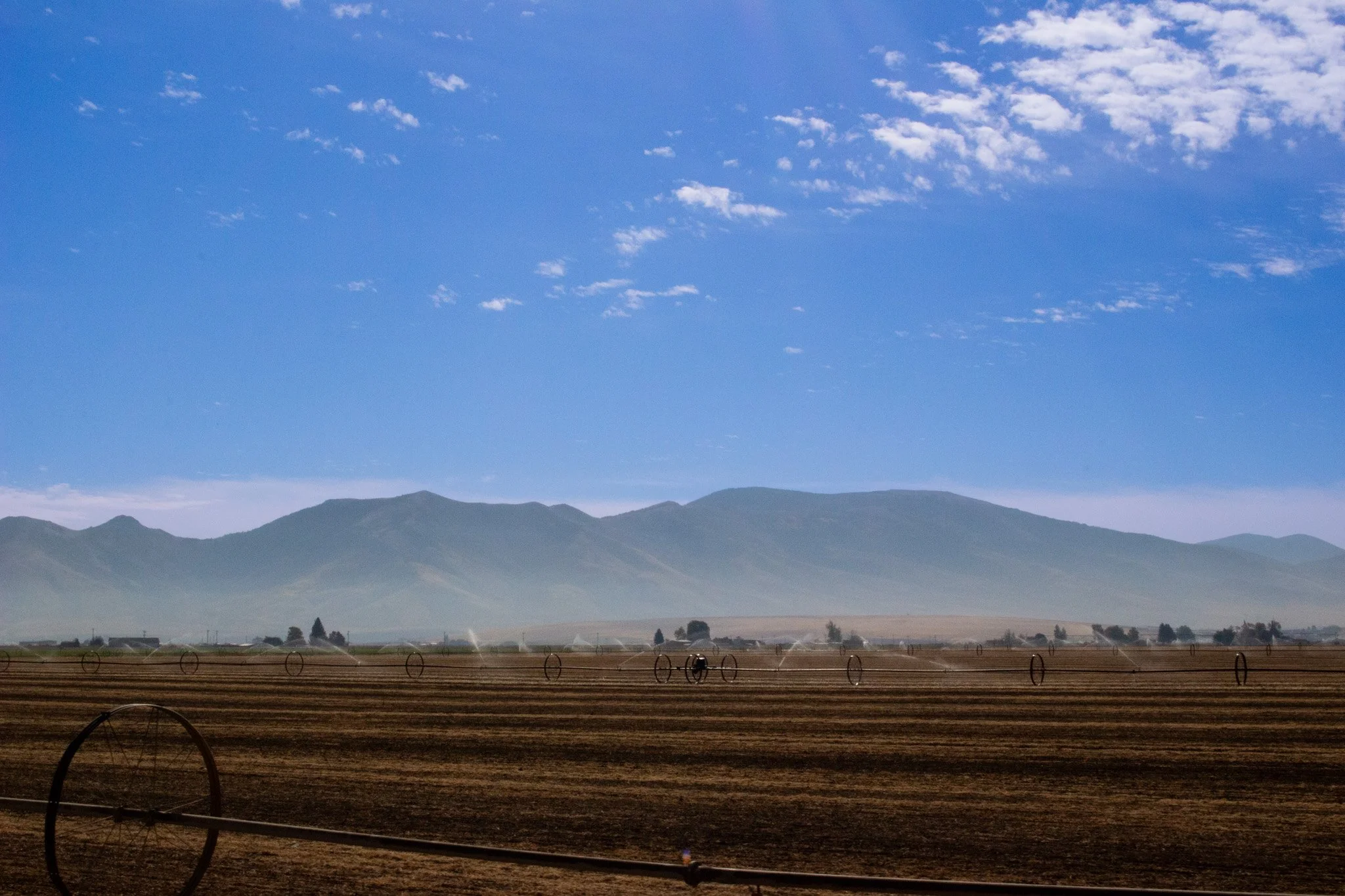 A landscape with a vast, open field, mountains in the background, and a blue sky with scattered clouds.