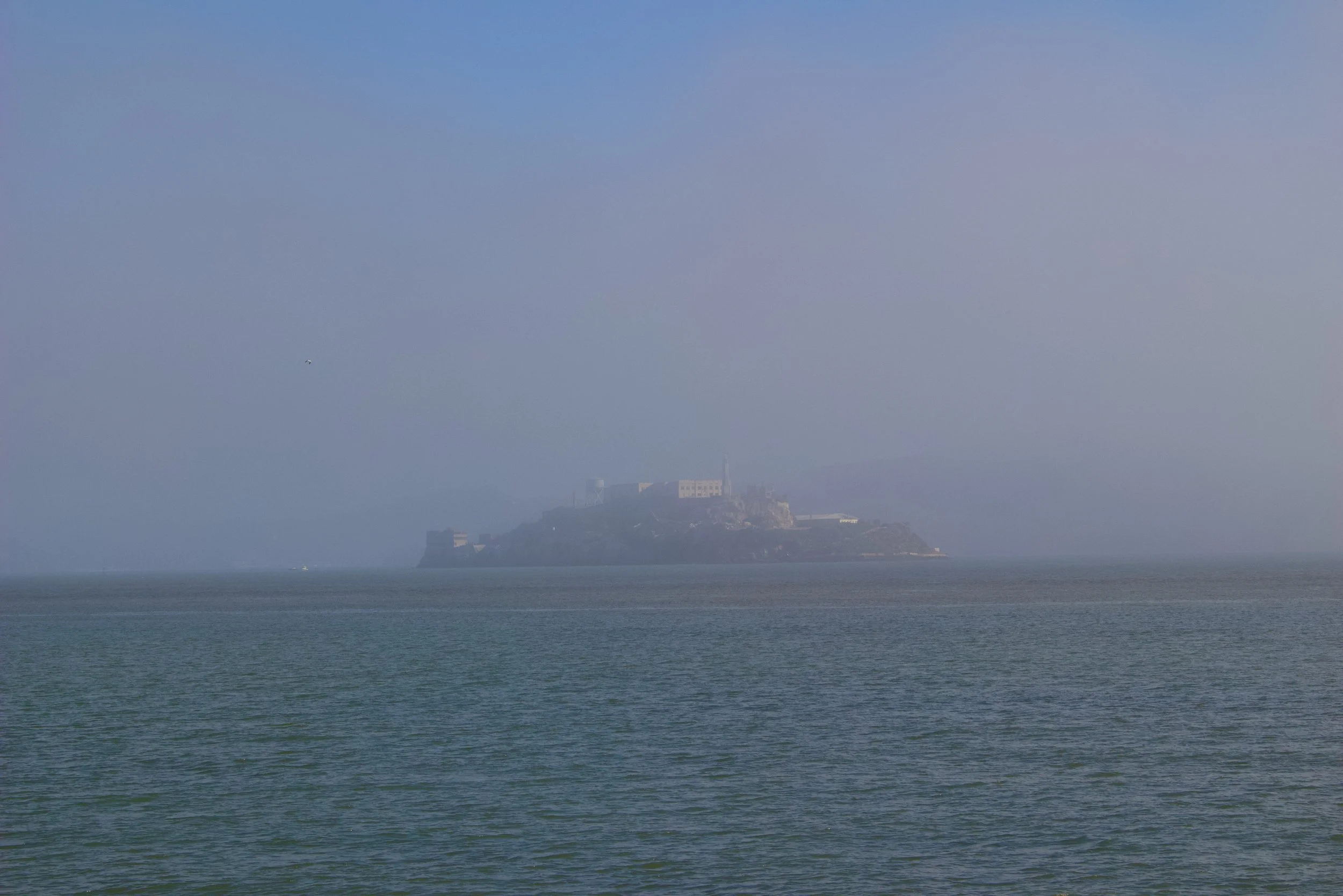 View of Alcatraz Island with foggy sky and calm waters in the foreground.
