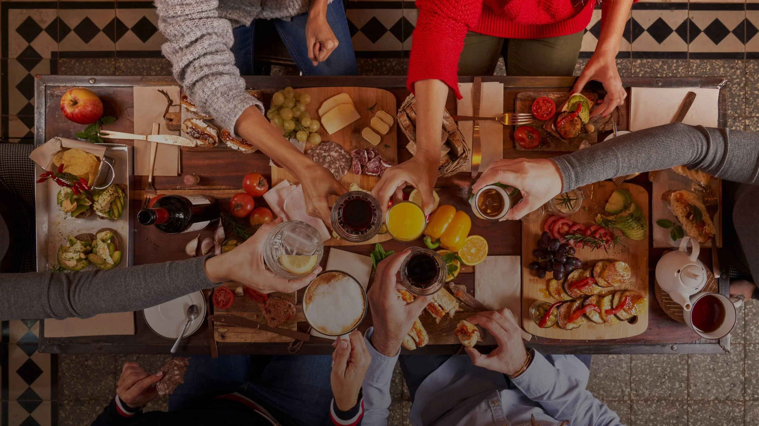 Top-down view of a group of people enjoying a shared meal with various dishes, drinks, and cutlery on a wooden table.