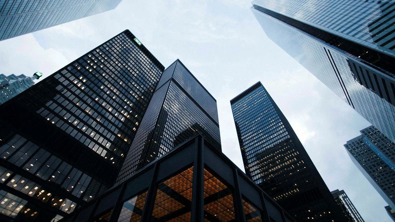 View of tall modern office buildings in a city from a low angle, with a cloudy sky in the background.
