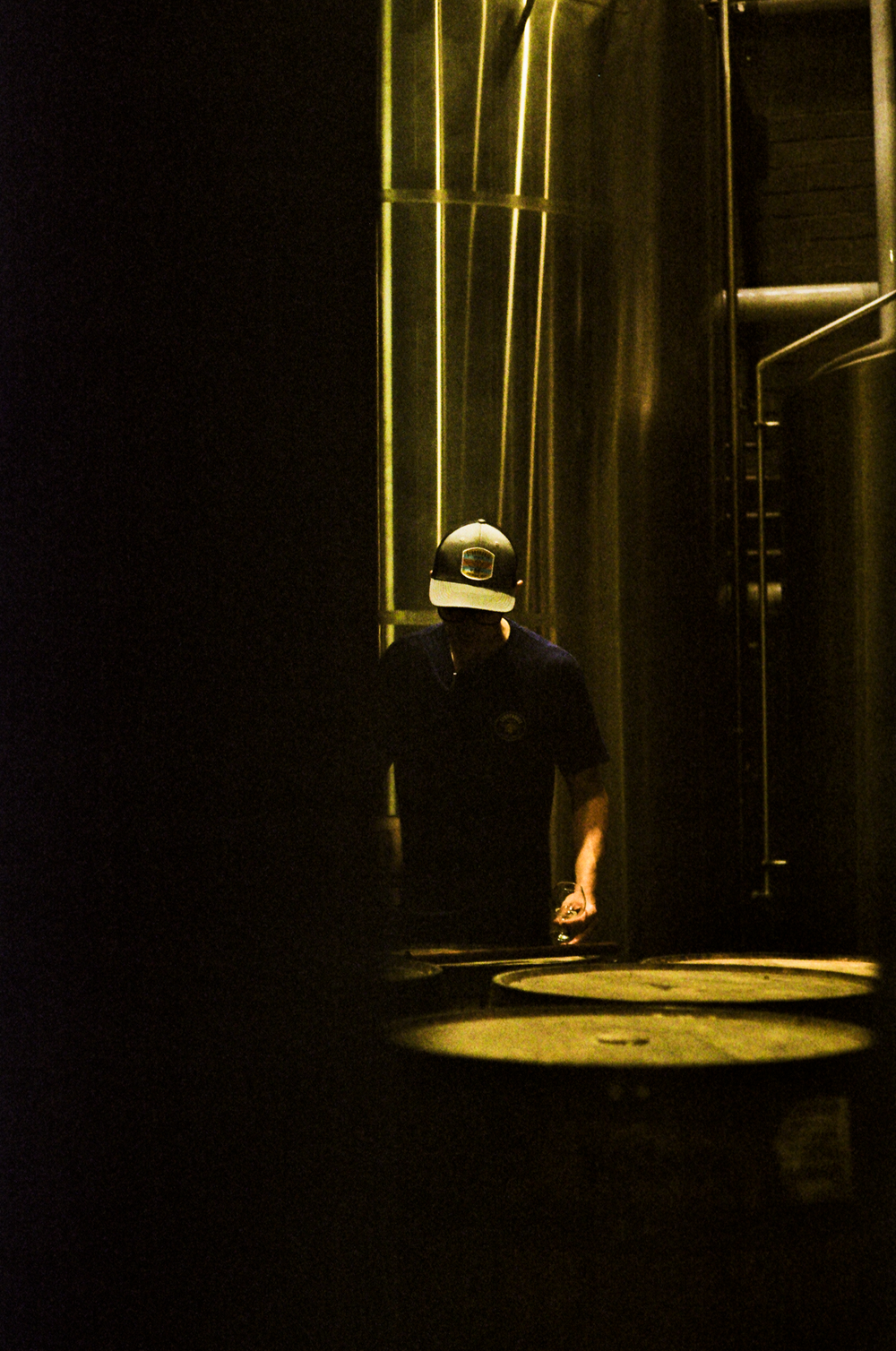 A silhouette at a barrel under a sliver of light at Storyhouse Spirits in East Village, shot on 35mm film