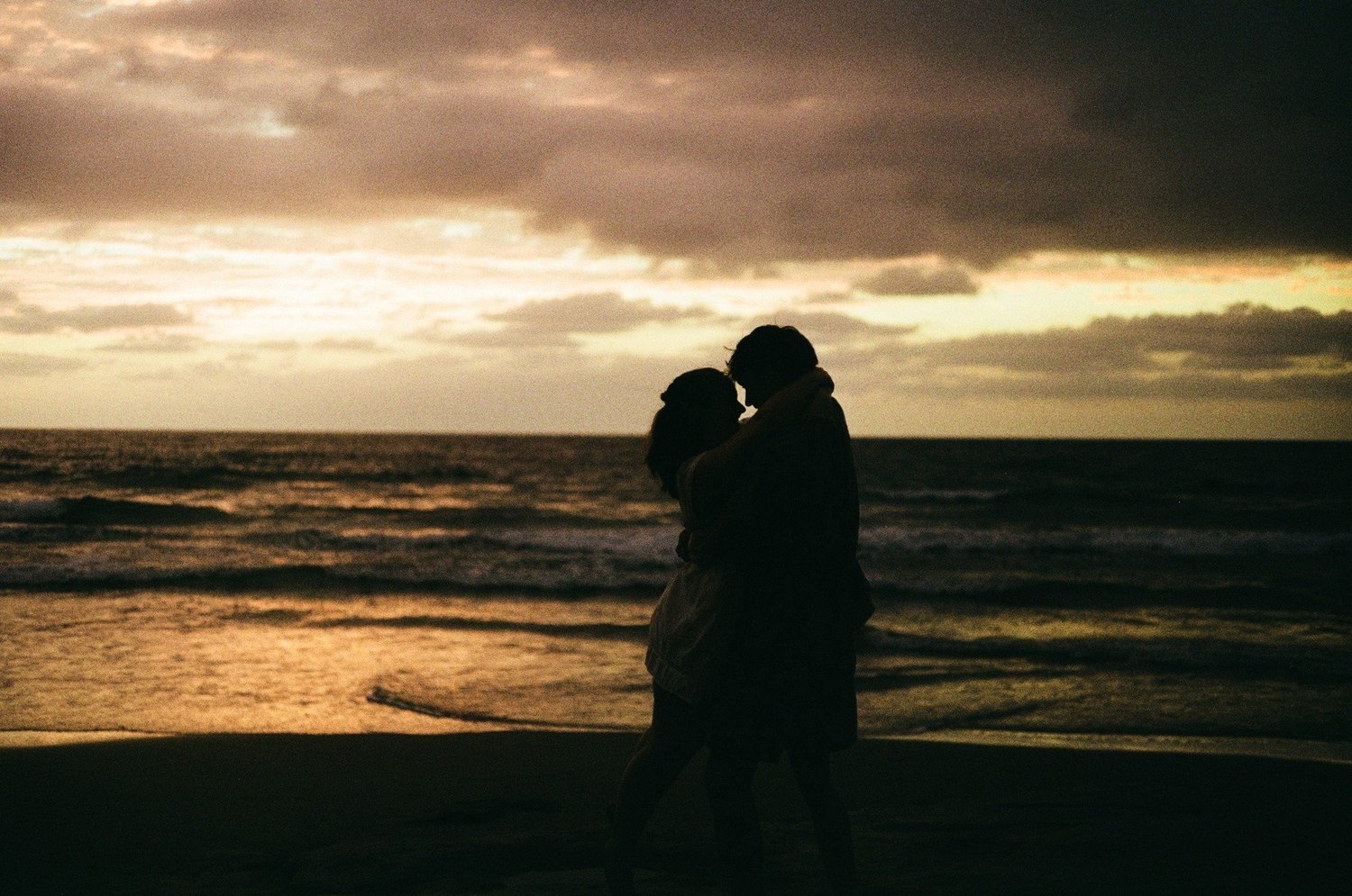 Rose and Brady in silhouette against the sunset over the ocean, shot on film