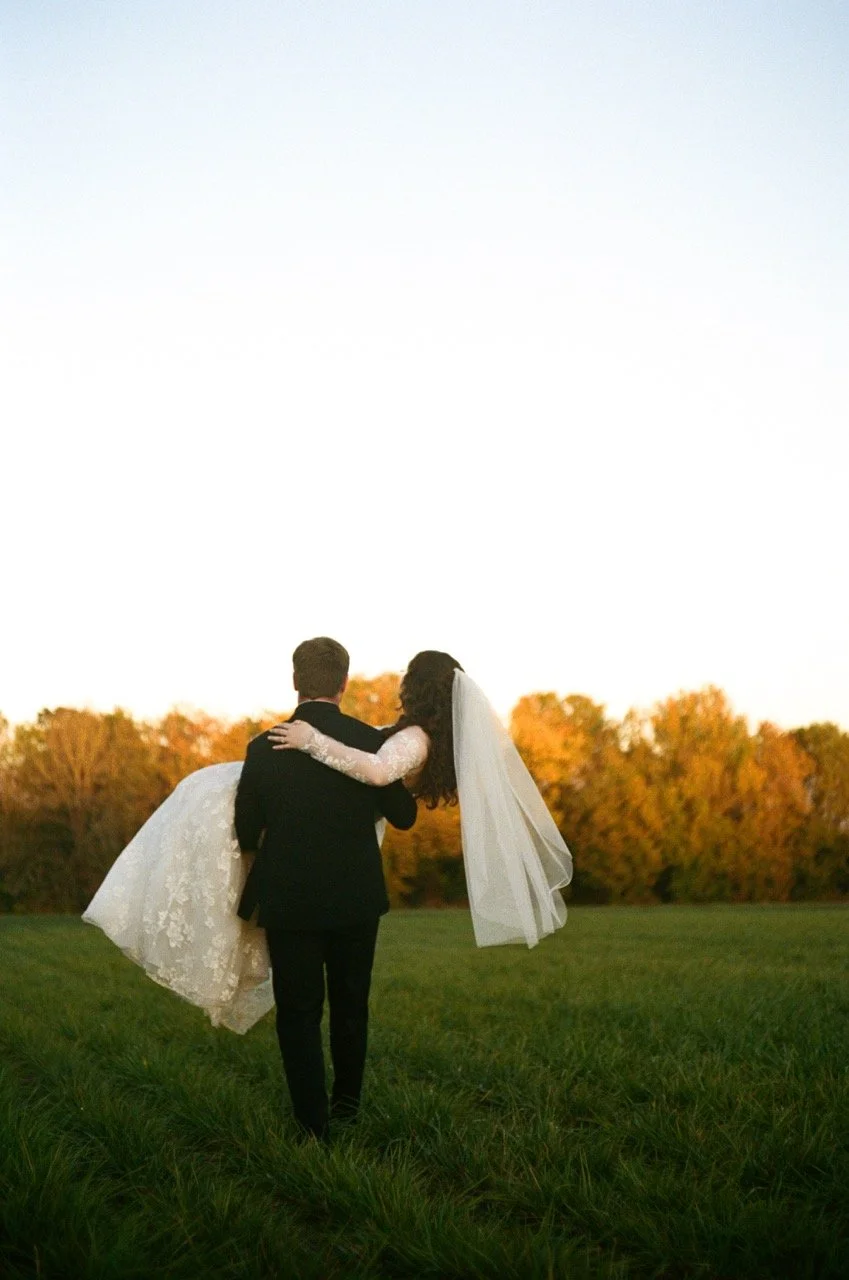 Preston lifting Carley in the field with fall trees behind them, shot on film